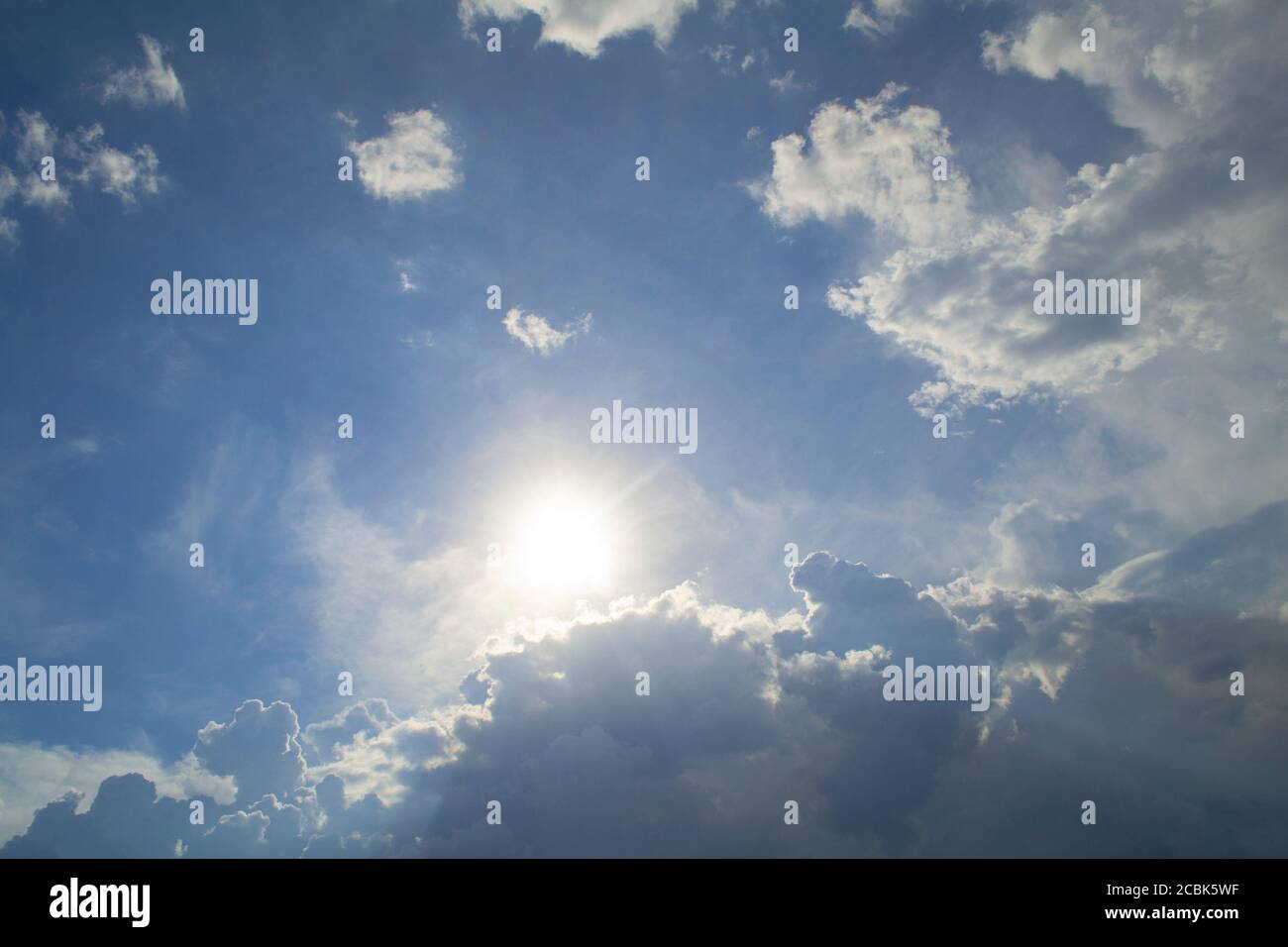 Blauer Himmel mit Wolken und Sonne im Zentrum. Die Sonne guckt hinter den Wolken hervor Stockfoto