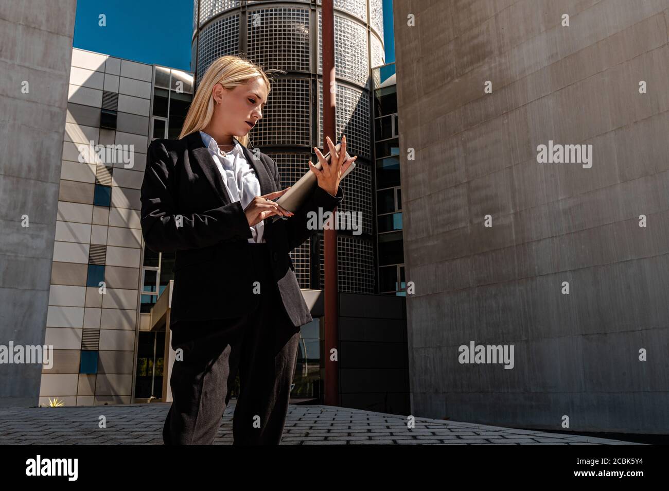 Eine junge kaukasische blonde Geschäftsfrau in formeller Kleidung Lesung Dokumente, während sie außerhalb des Gebäudes stehen Stockfoto