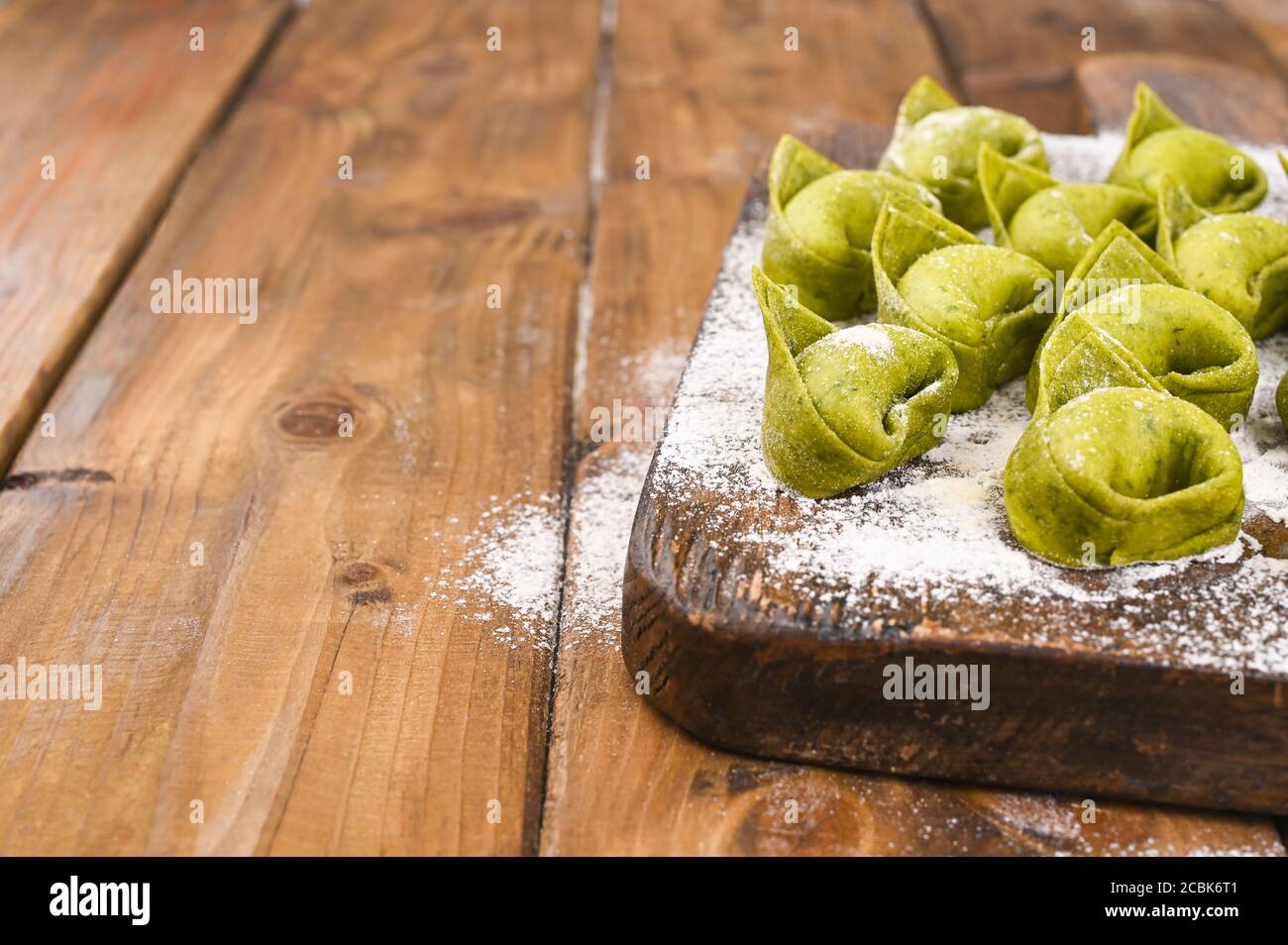 Tortellini e Tortelloni typische Gerichte emilia italien. Food Hintergrund mit hausgemachten rohen italienischen Tortelloni und Zutaten für grünes Pesto auf Holzhintergrund . Weitwinkelansicht. Speicherplatz kopieren. Stockfoto