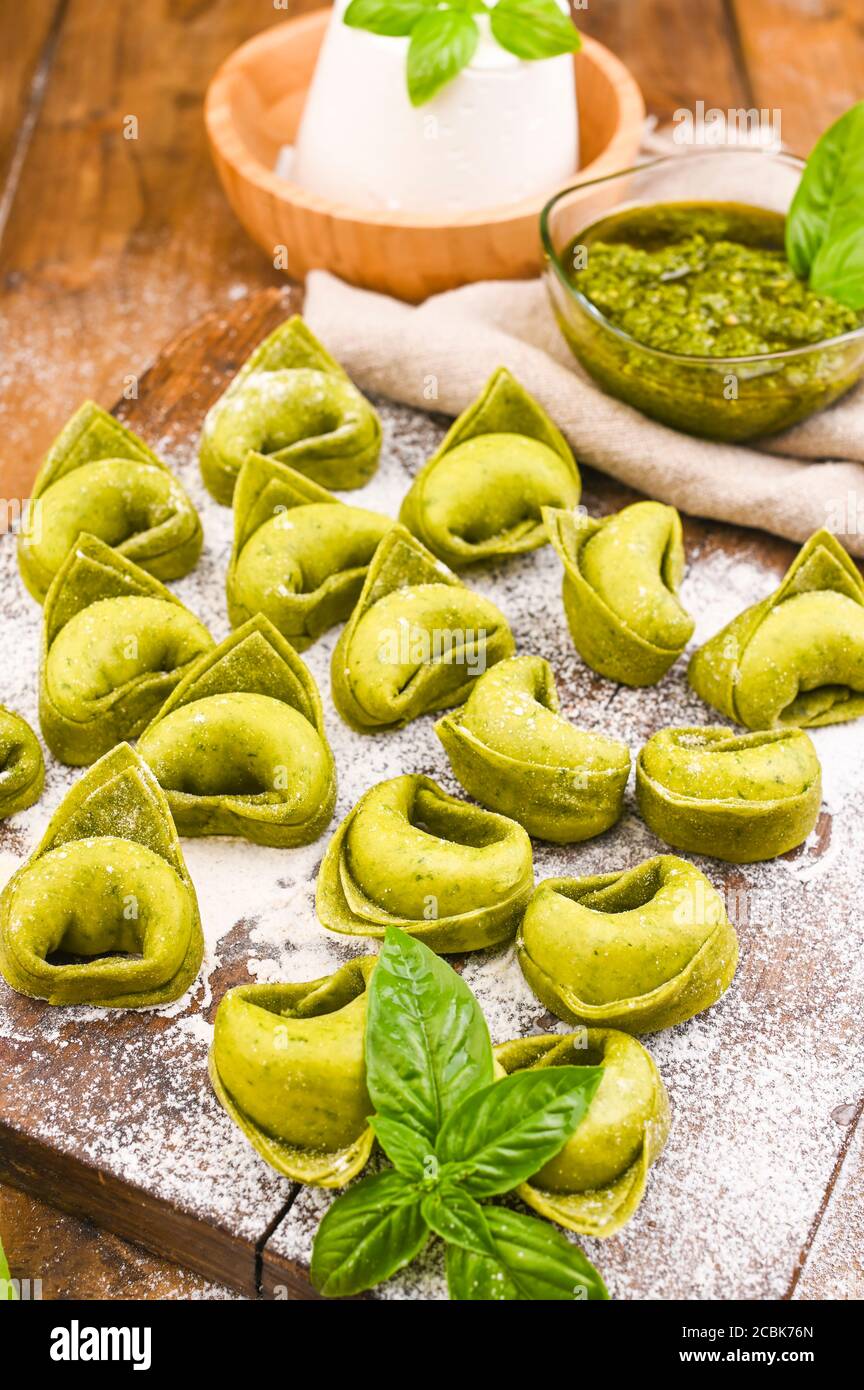 Tortellini e Tortelloni typische Gerichte emilia italien. Food Hintergrund mit hausgemachten rohen italienischen Tortelloni und Zutaten für grünes Pesto auf Holzhintergrund . Weitwinkelansicht. Speicherplatz kopieren. Stockfoto