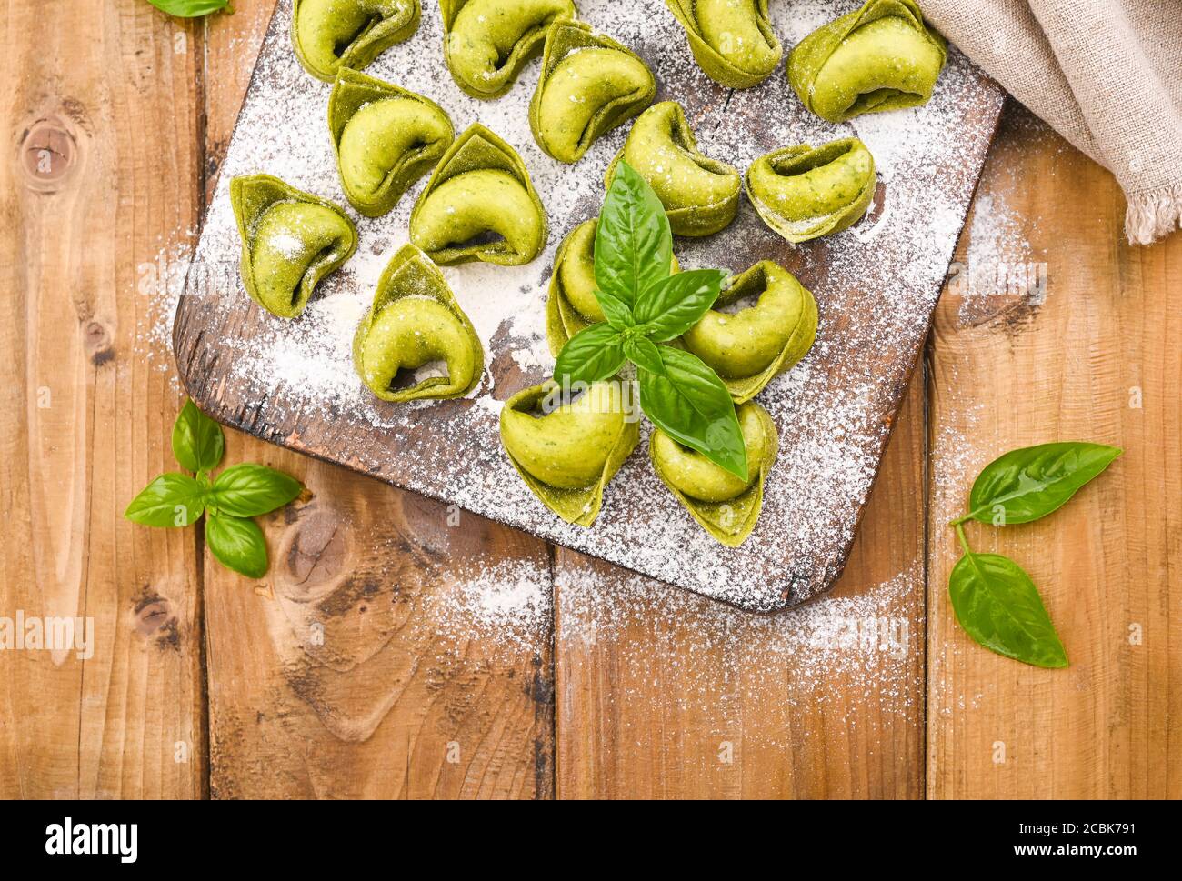 Tortellini e Tortelloni typische Gerichte emilia italien. Food Hintergrund mit hausgemachten rohen italienischen Tortelloni und Zutaten für grünes Pesto auf Holzhintergrund . Weitwinkelansicht. Speicherplatz kopieren. Stockfoto