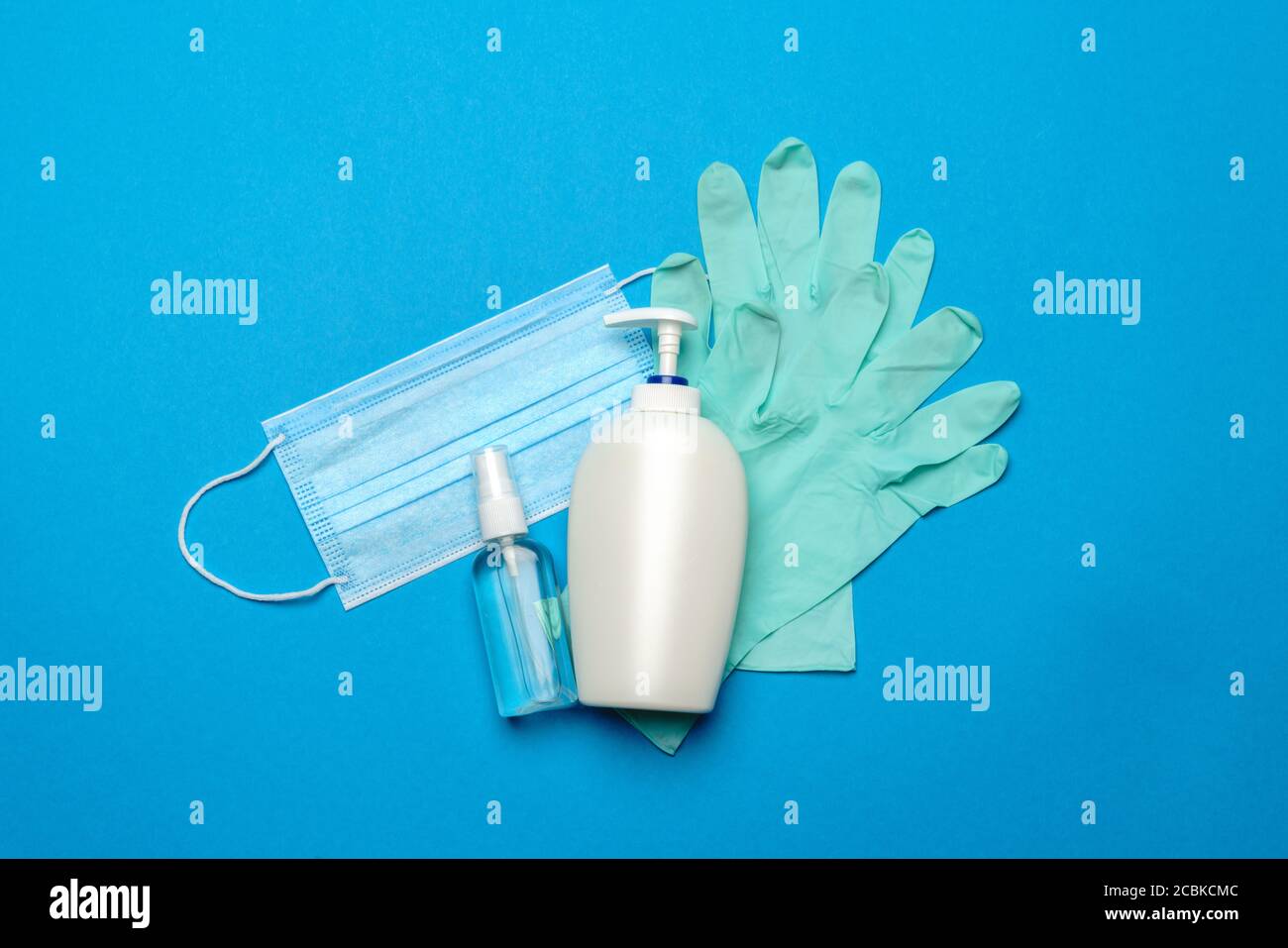 Einweg-blaue medizinische Gesichtsmaske, Gummi-Latex-Handschuhe und Alkohol Hand Desinfektionsmittel antiseptisch auf blauem Hintergrund Stockfoto