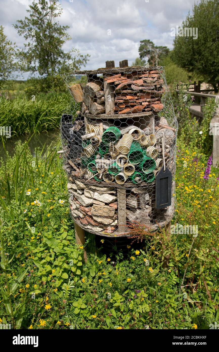 Großes Insektenhotel aus alten Lehmpfeifen, pastigem Korrugata-Rohr, Ziegel und Holz inmitten von Wildblumen im Wildflower und Wetland Trust, Slimbri Stockfoto