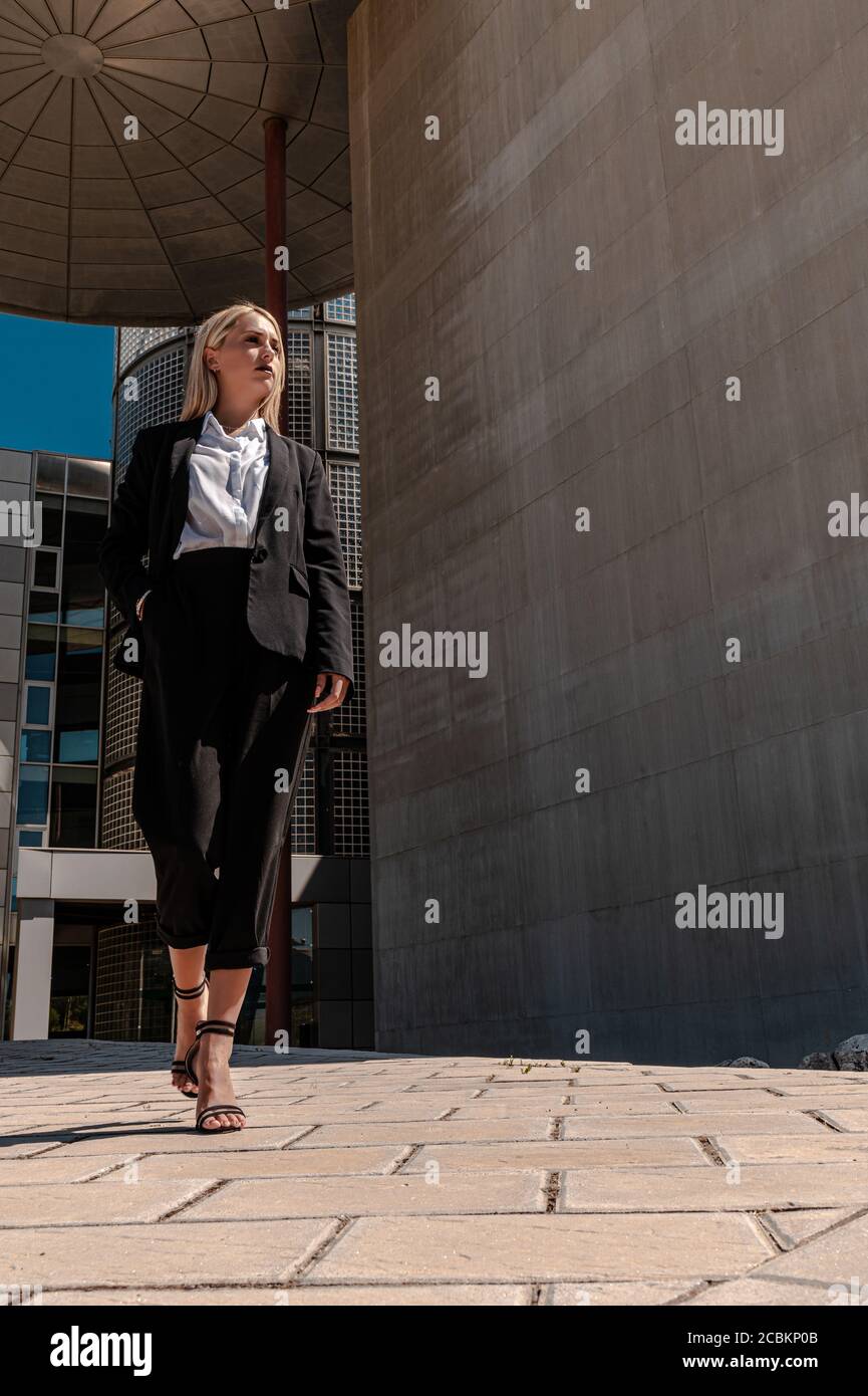 Eine vertikale Aufnahme einer jungen blonden Geschäftsfrau in Formelle Kleidung zu Fuß in der Nähe des Gebäudes Stockfoto