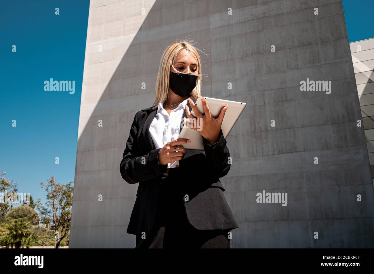 Eine junge kaukasische blonde Geschäftsfrau in formeller Kleidung und Eine Gesichtsschutzmaske zum Lesen von Dokumenten, während Sie außerhalb des stehen Gebäude Stockfoto
