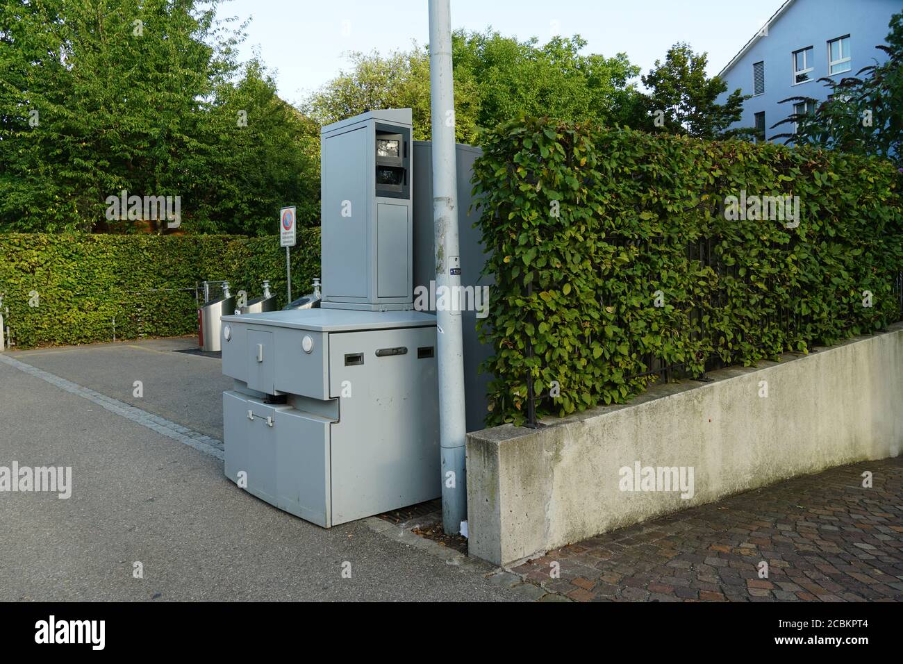 Verkehrserzwingungskamera, Verkehrssicherheitskamera oder Fotoradar in der Schweiz versteckt sich die Straße hinter dem grünen Heckenzaun und der Straßenlaterne Stockfoto