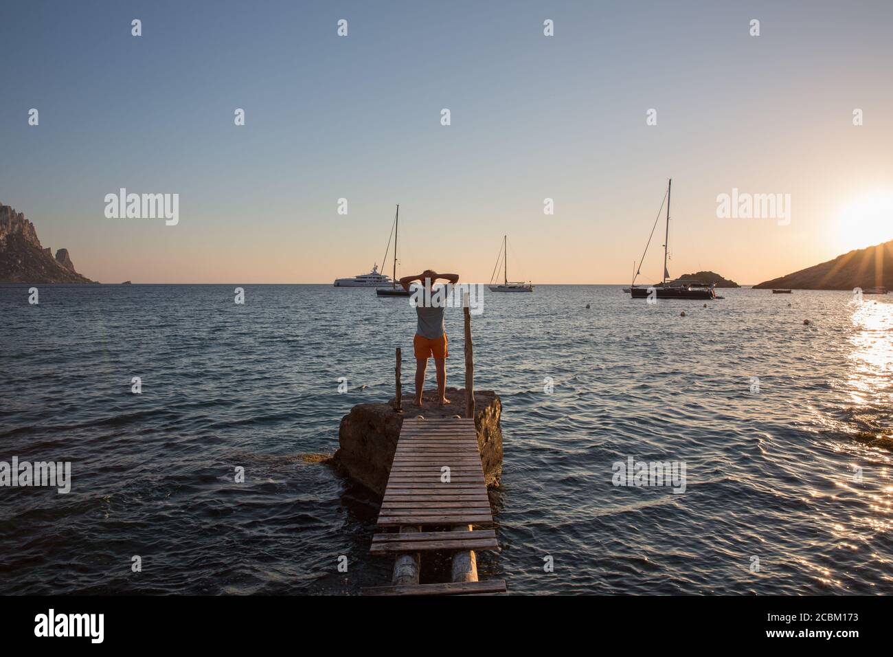 Junger Mann, der bei Sonnenuntergang auf dem alten Pier steht, Ibiza, Spanien Stockfoto