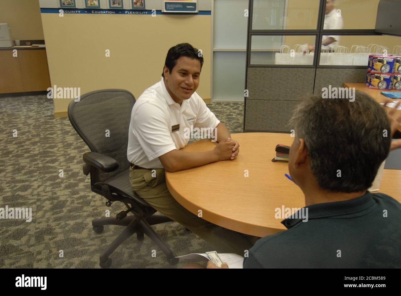 Austin, TX, 1. August 2006: Der hispanische Kundendienstmitarbeiter hilft einem Kunden bei der Eröffnung eines Kontos während der großen Eröffnungsveranstaltung für eine Zweigstelle einer Capital One Bank in einem schnell wachsenden Vorort. ©Bob Daemmrich Stockfoto