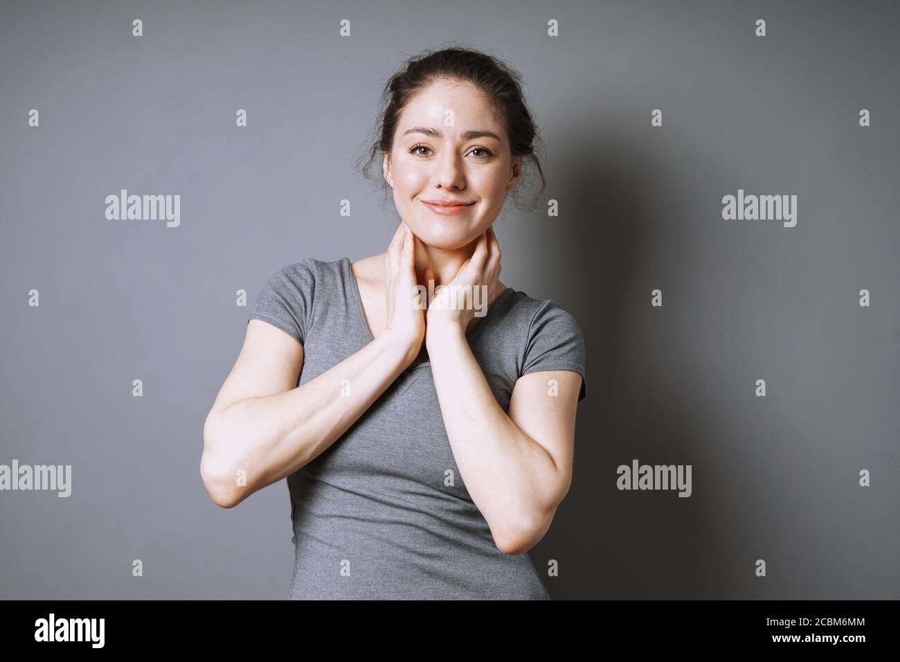 Glückliche junge Frau mit einem zufriedenen Lächeln auf ihrem Gesicht Vor grauem Hintergrund mit Kopierplatz Stockfoto