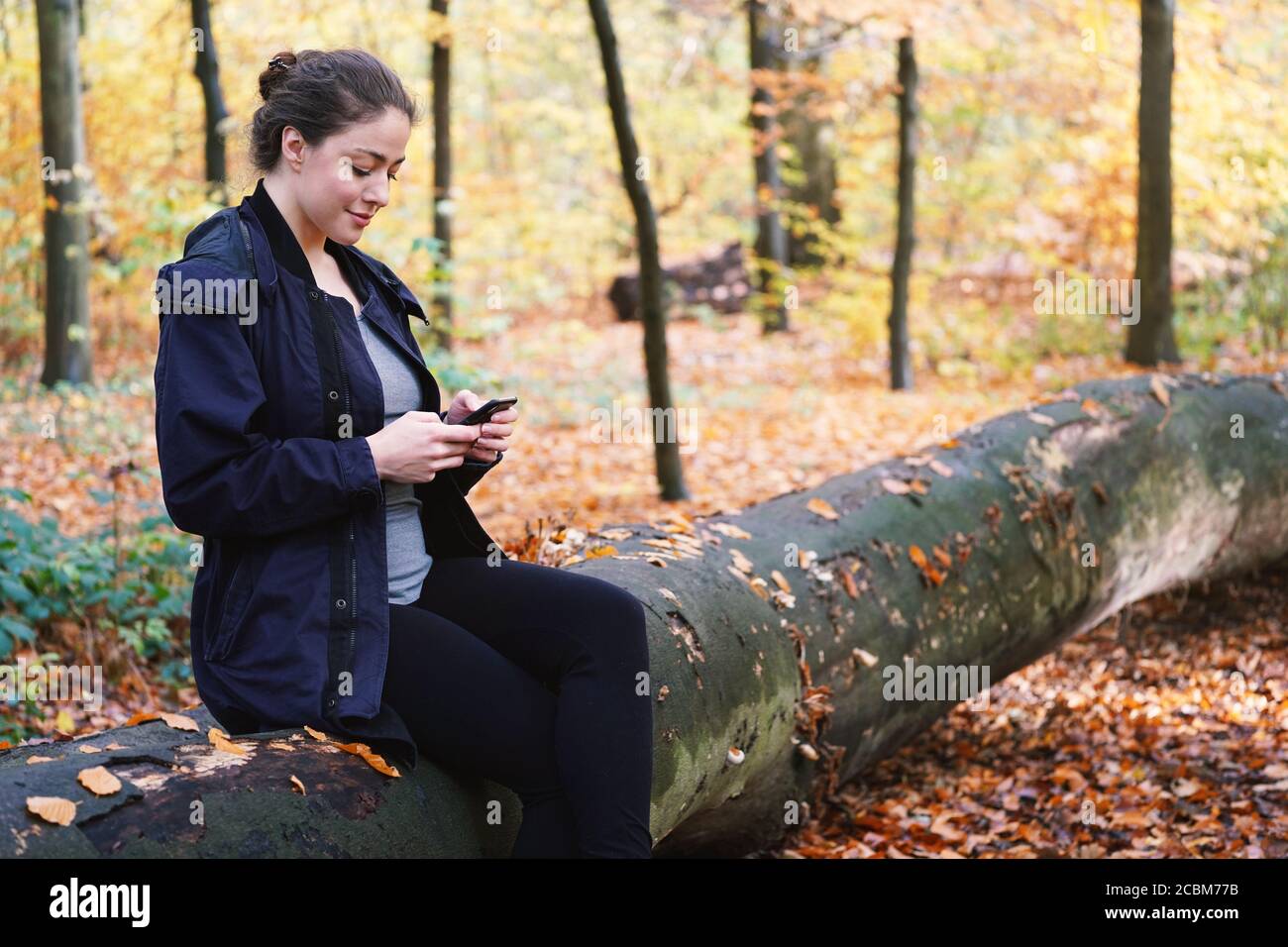 Junge Frau in den Zwanzigern mit dem mobilen Smartphone während der Ruhe Im Freien im Wald Stockfoto