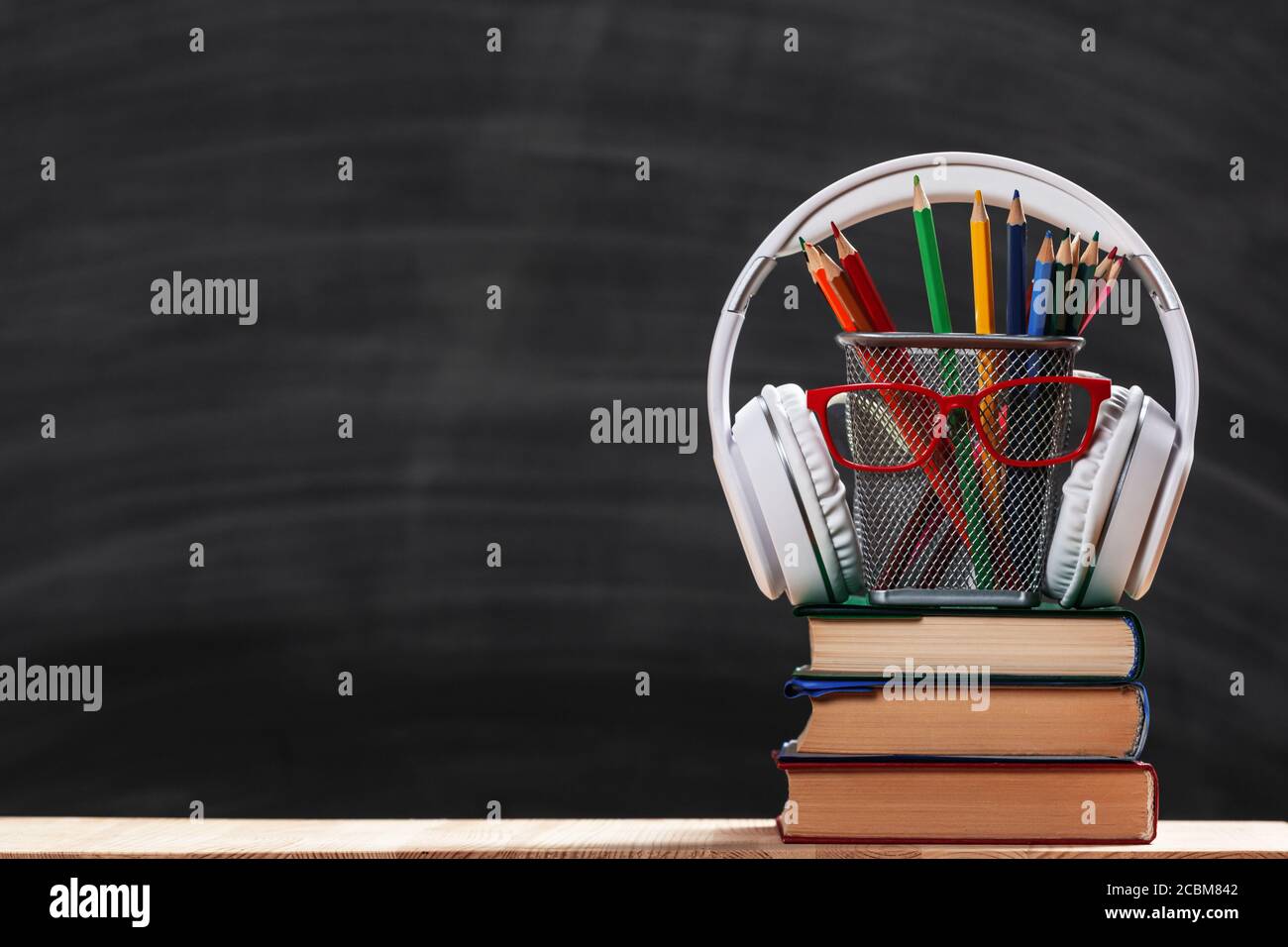 Zurück zur Schule. Komposition aus einem Stapel von Büchern Bleistifte Brille Kopfhörer auf einem schwarzen Kreidetafel Hintergrund. Tag des Lehrers. Stockfoto