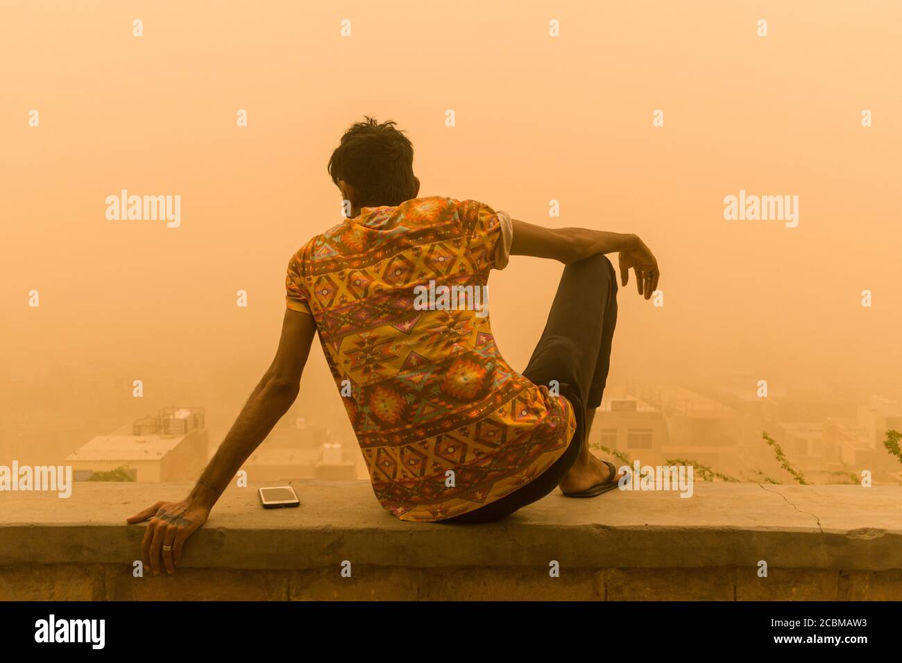 Mann, der auf der Stadtmauer sitzt und die Aussicht genießt Mitten im Sandsturm Stockfoto