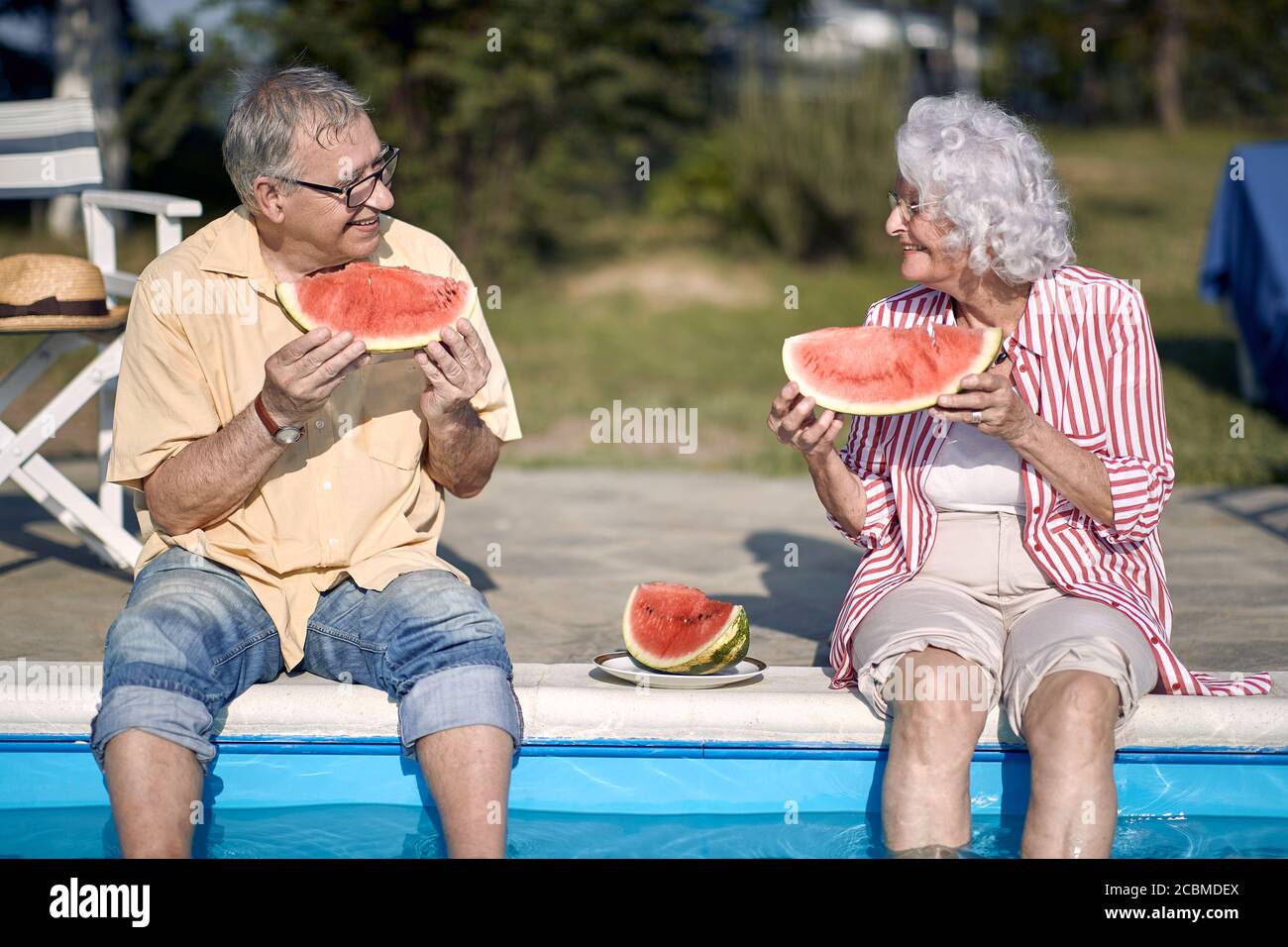 Ältere Paare essen Wassermelone am Pool.Mann und Frau genießen im Sommerurlaub. Stockfoto