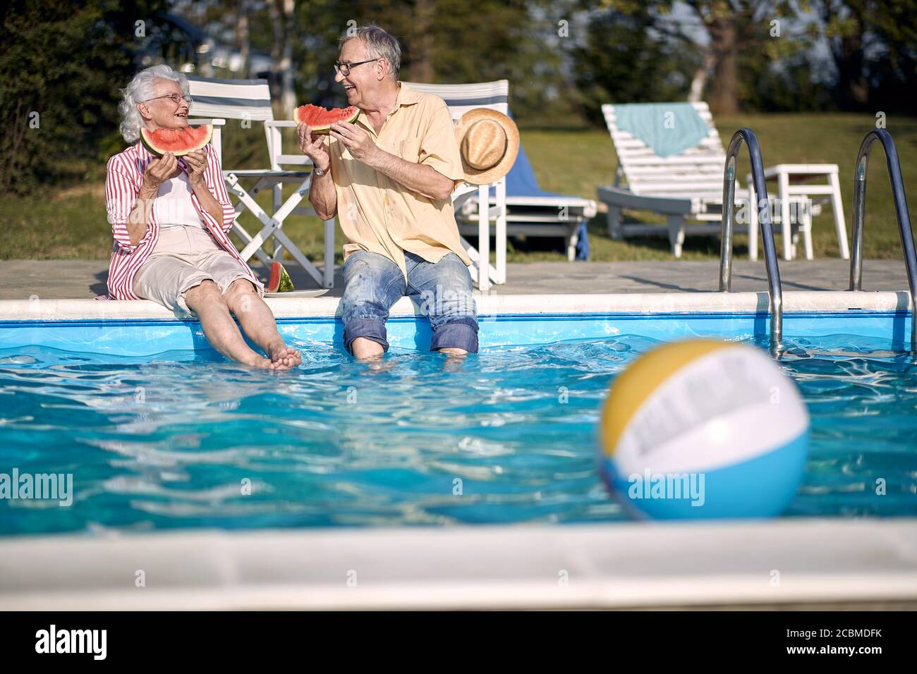Romantisches glückliches Seniorenpaar genießen Sie im Sommerurlaub in der Nähe von Schwimmbad und essen Wassermelone. Stockfoto