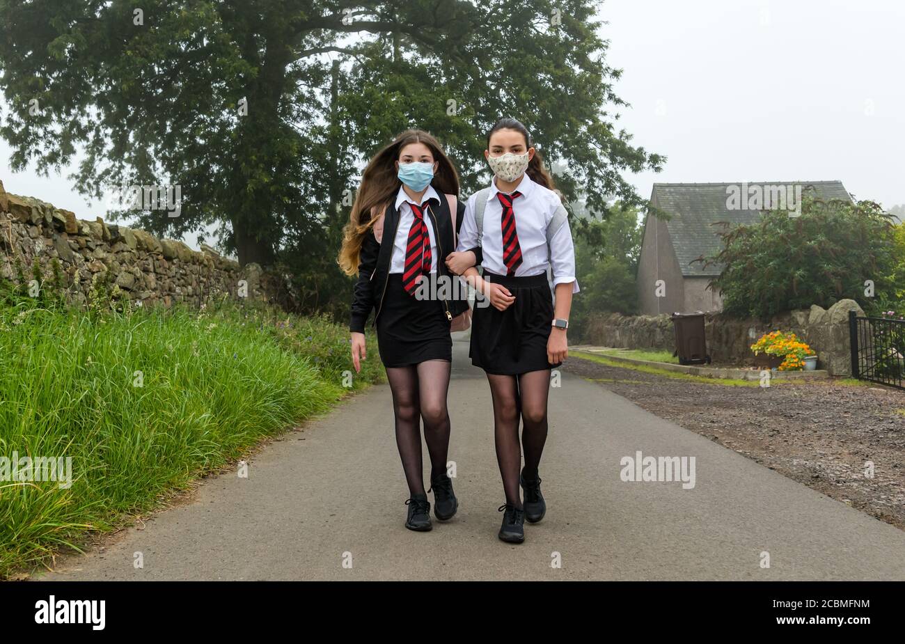Zwillingsmädchen verlassen ihr Zuhause mit Gesichtsmasken und beginnen den ersten Schultag nach der Aussperrung der Pandemie Covid-19, Schottland, Großbritannien Stockfoto