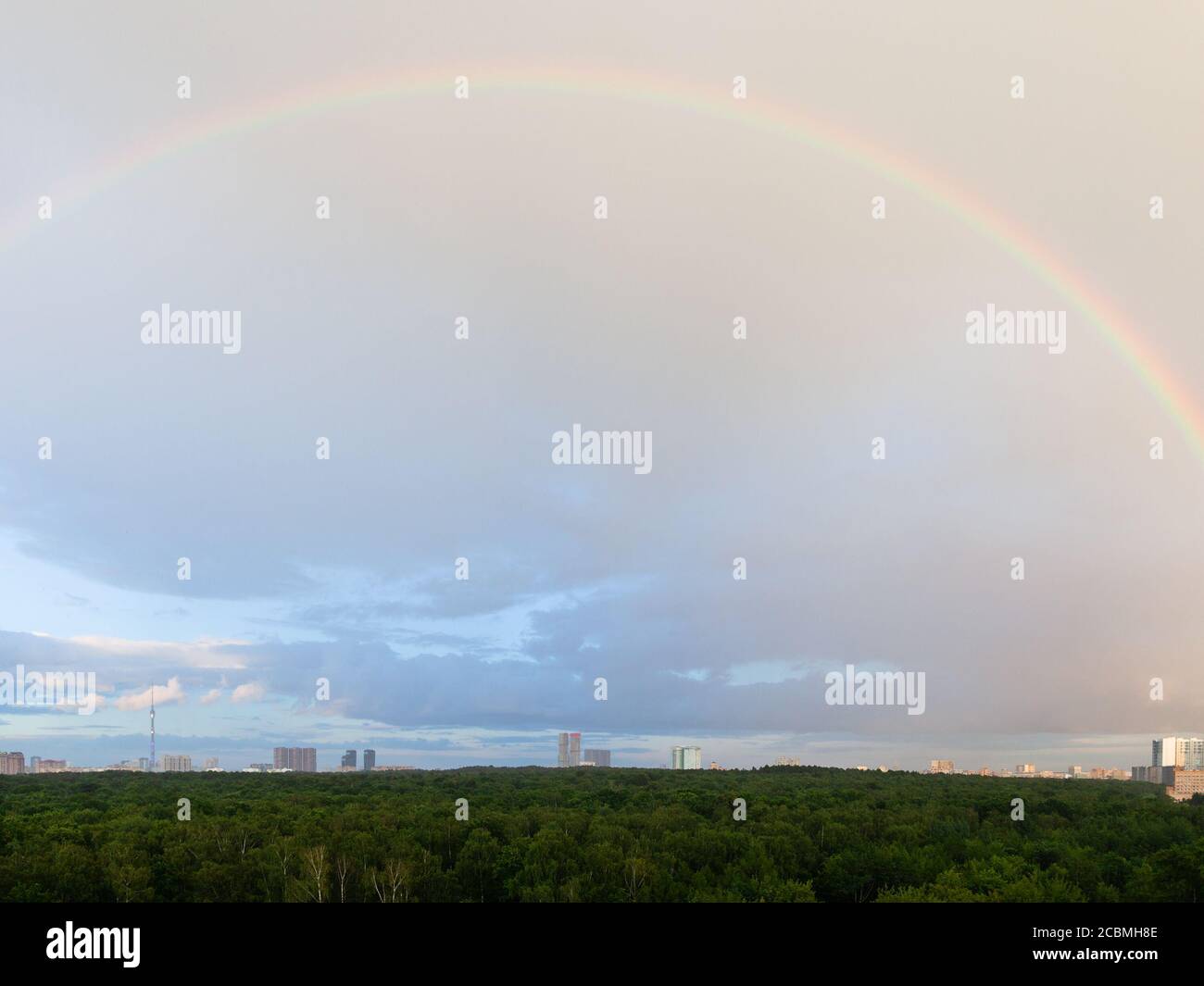 regenbogen in blau wolkigen Himmel über Stadtpark und Häuser Im sonnigen Sommerabend Stockfoto
