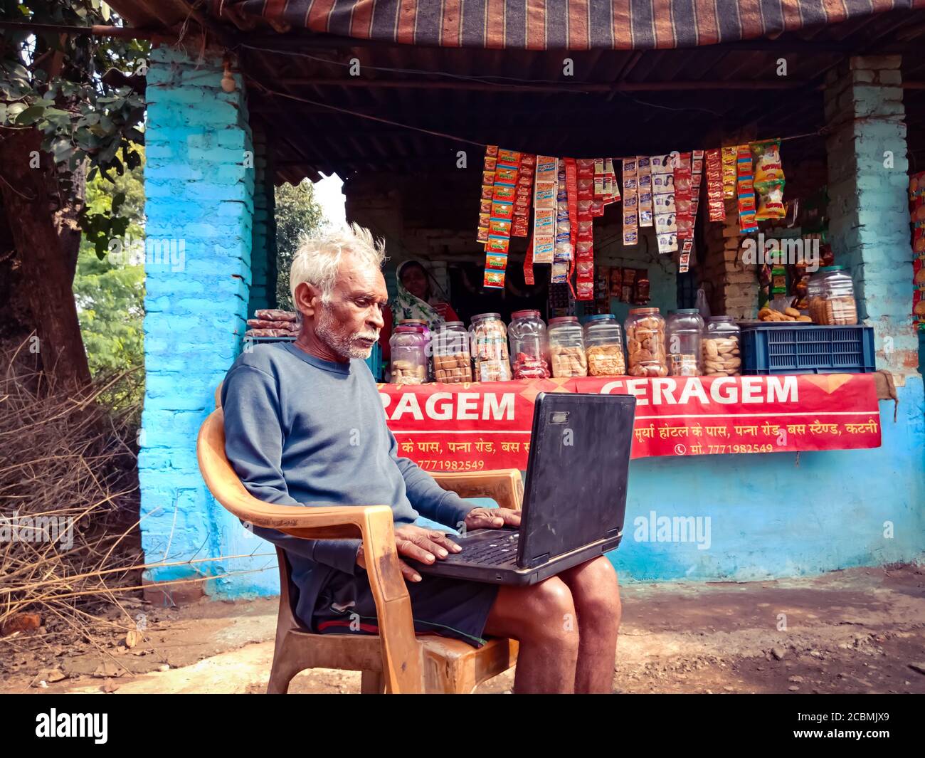 DISTRIKT KATNI, INDIEN - 01. JANUAR 2020: Ein indischer alter Mann, der Laptop-Computer betreibt, der auf einem Stuhl im Hintergrund des offenen Bereichs sitzt. Stockfoto