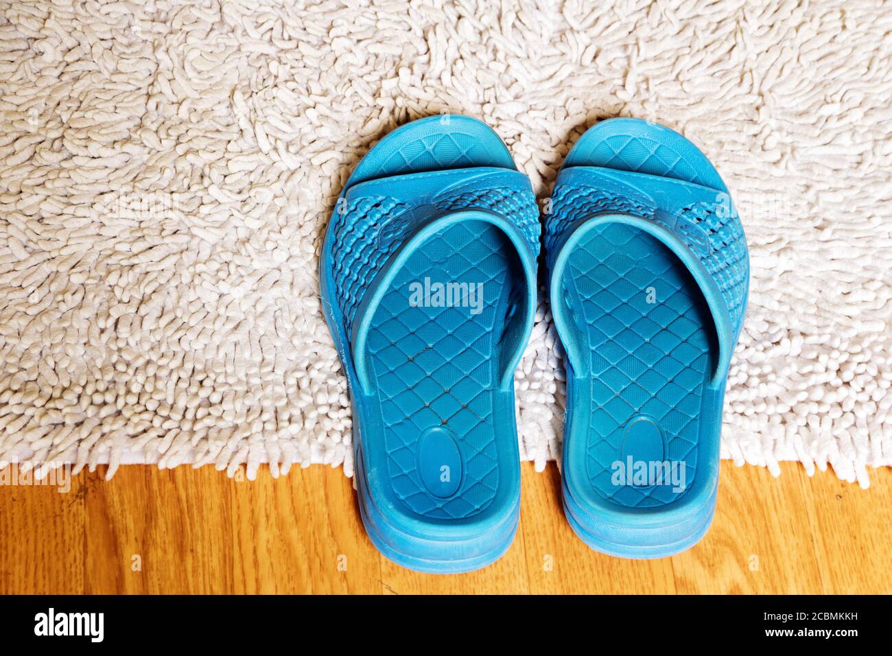 Damen innen blauen Gummi Hausschuhe auf einem weichen weißen Teppich. Stockfoto
