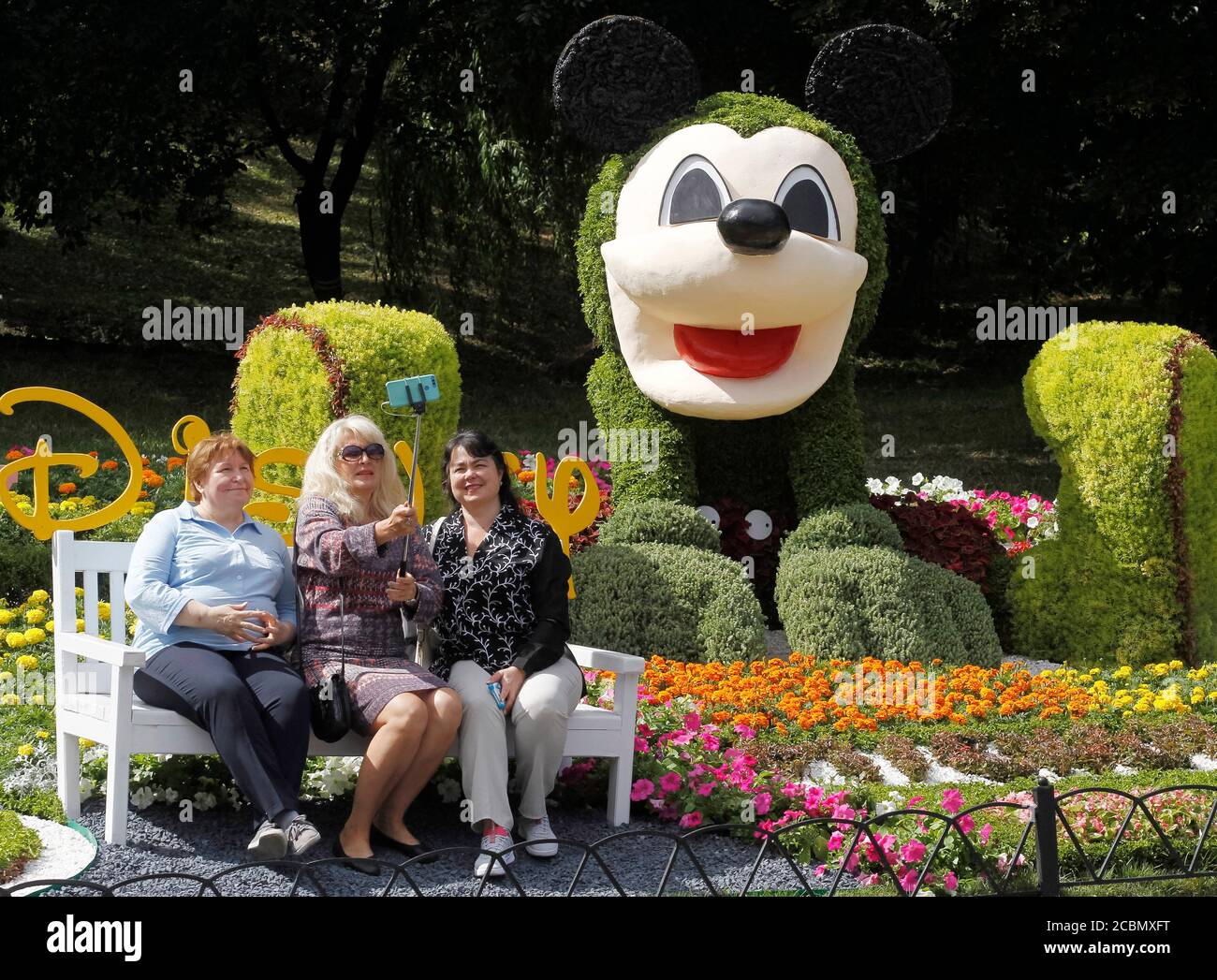 Frauen machen während der Ausstellung ein Selfie neben einer Mickey Mouse Zeichentrickfigur.über 300 Tausend Blumen wurden verwendet, um bekannte Zeichentrickfiguren und Spots für Selfies in einer Cartoons Land Blumen Ausstellung zu erstellen. Stockfoto