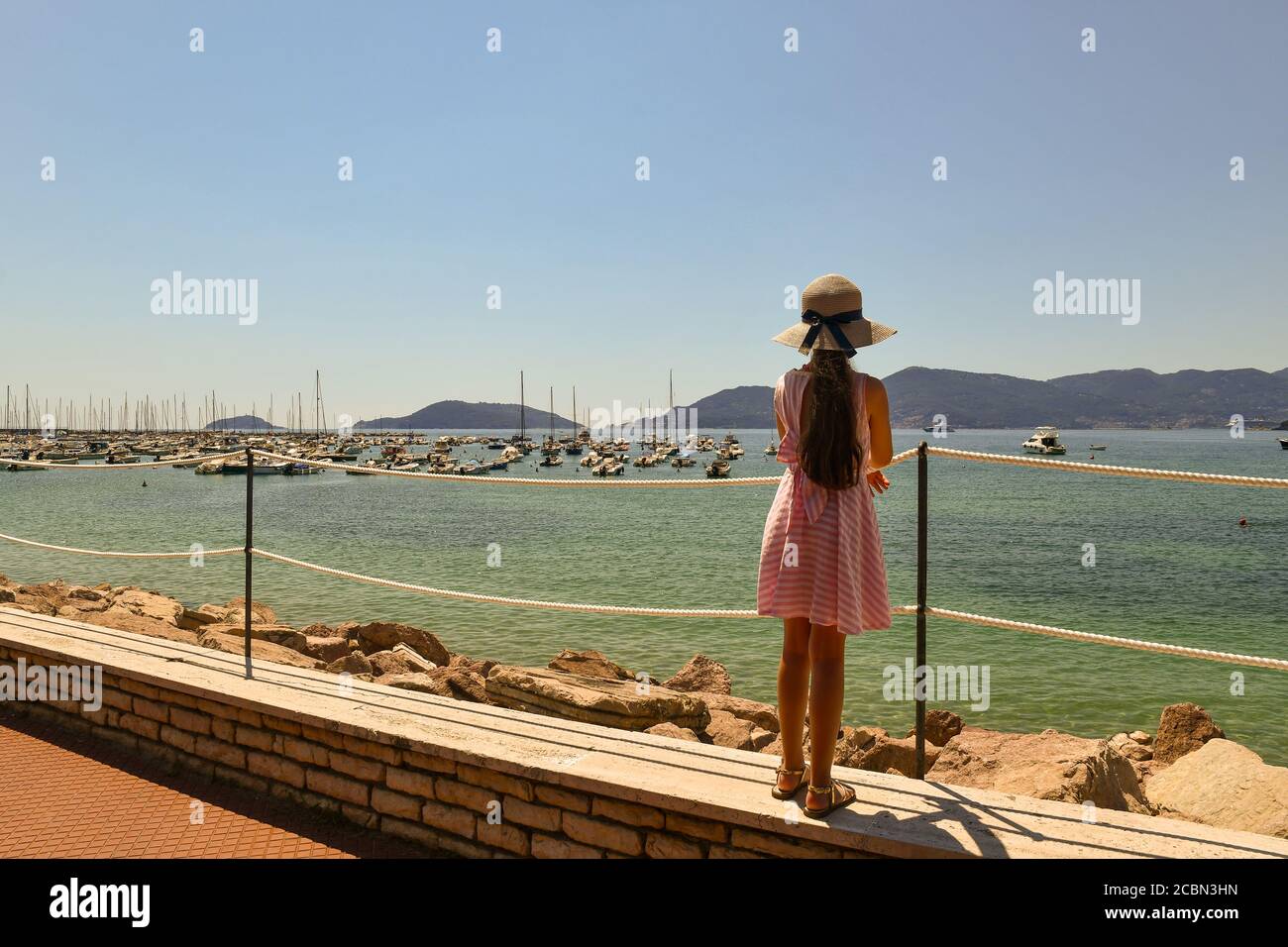 Ein langhaariges kleines Mädchen (9-10 J.) von hinten bewundert den Golf der Dichter mit dem Vorgebirge von Porto Venere im Sommer, Lerici, La Spezia, Italien Stockfoto