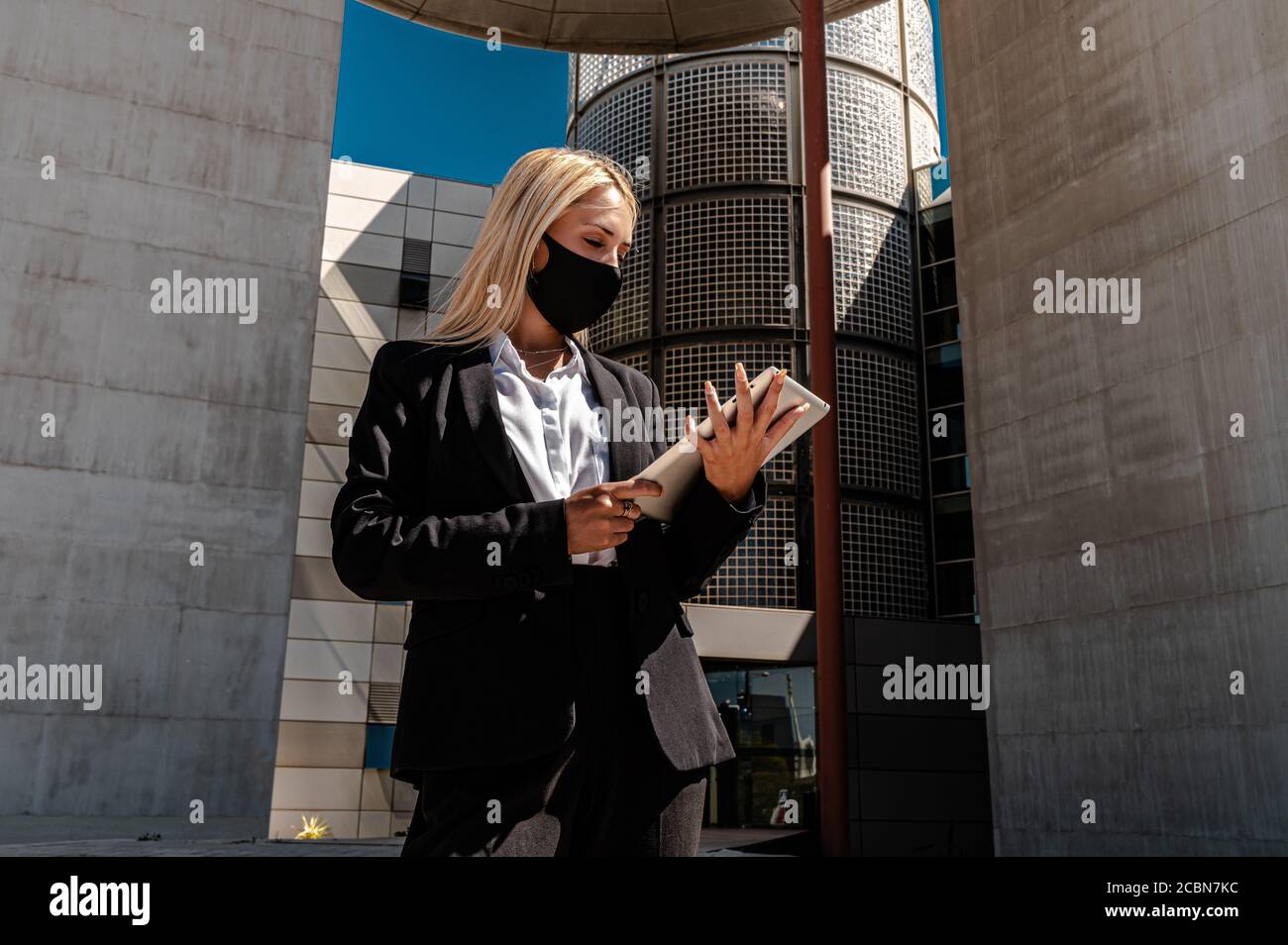 Eine junge kaukasische blonde Geschäftsfrau in formeller Kleidung und Eine Gesichtsschutzmaske zum Lesen von Dokumenten, während Sie außerhalb des stehen Gebäude Stockfoto
