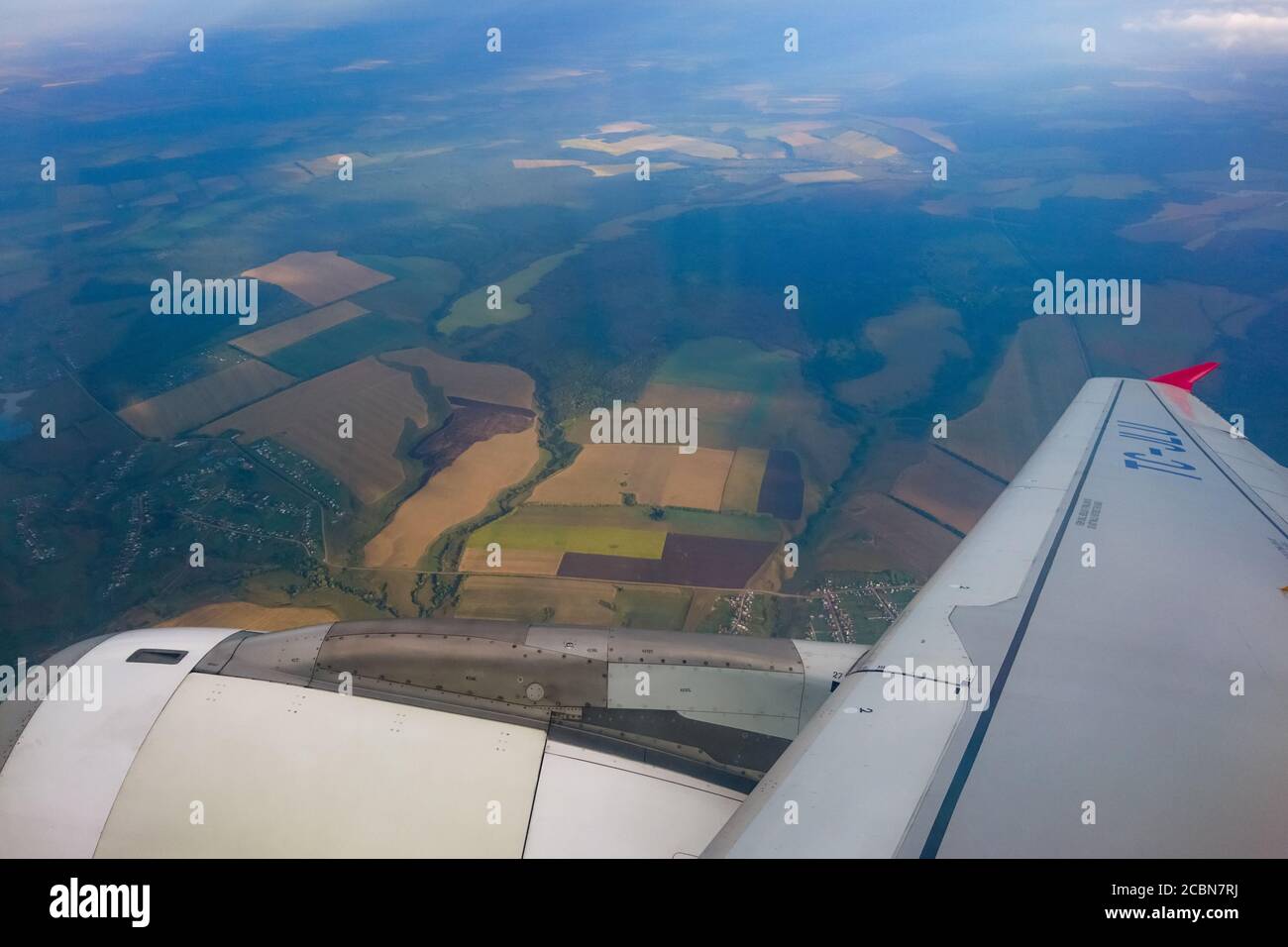 Blick vom Flugzeug-Illuminator. Der Blick aus dem Fenster des Flugzeugs auf den Flügel, die Erde und die Felder. Stockfoto