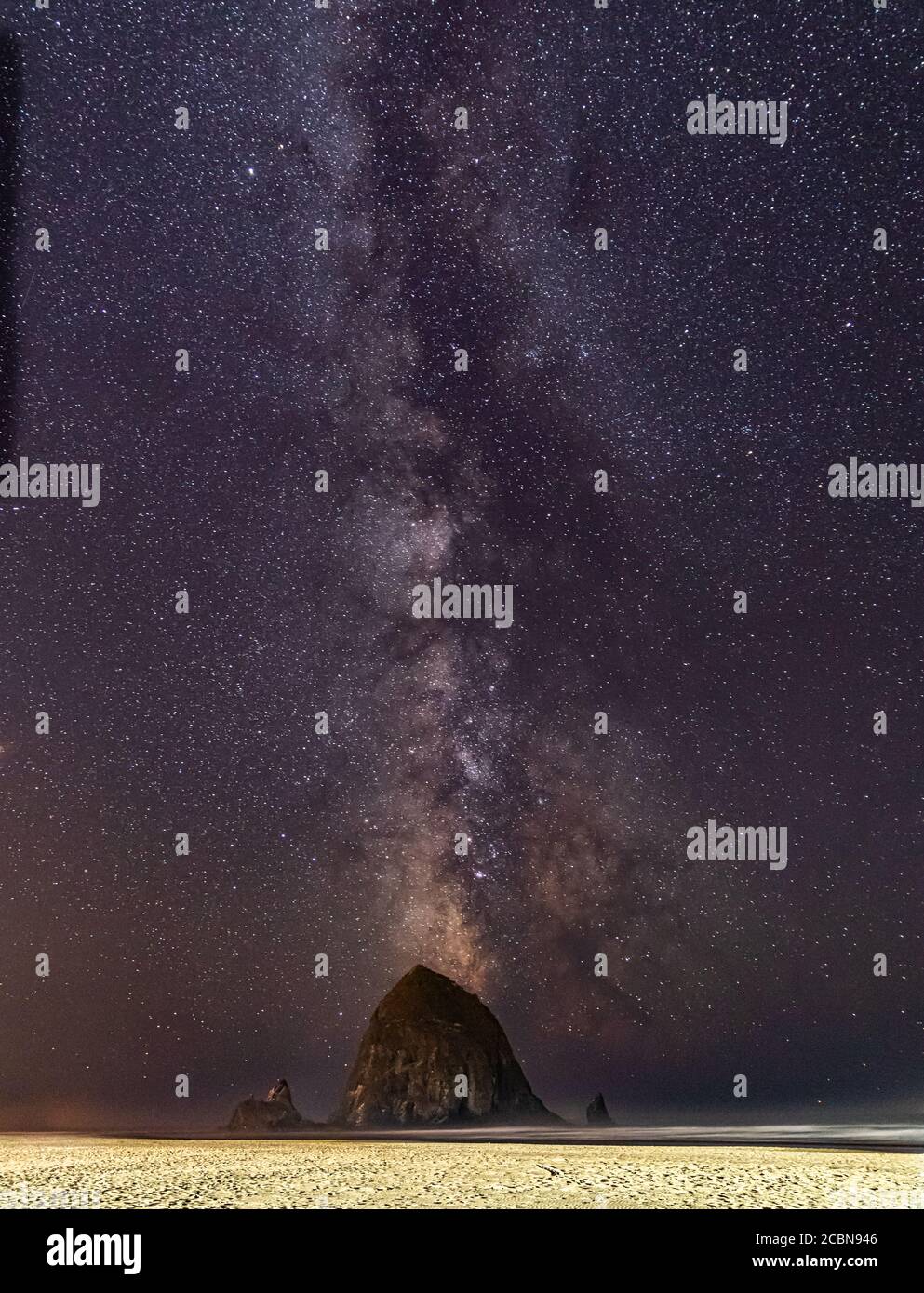 Vertikales Foto - Milchstraße scheint in den Himmel über Haystack Rock am Cannon Beach in Oregon Stockfoto