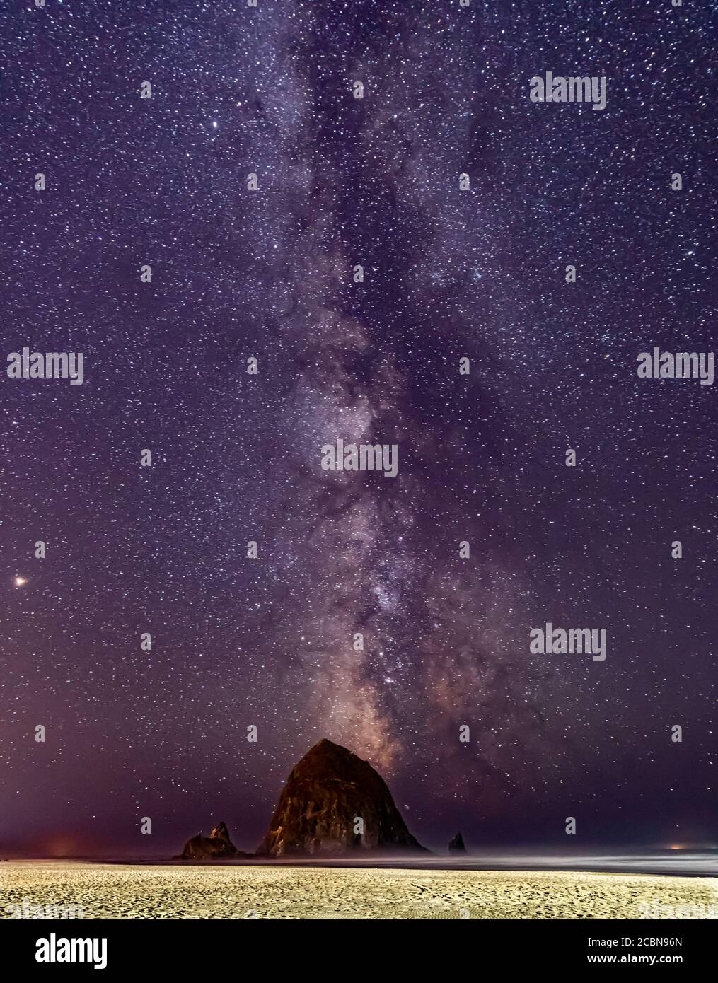 Vertikales Bild-Milchstraße leuchtet im Himmel über Haystack Rock Am Cannon Beach in Oregon Stockfoto