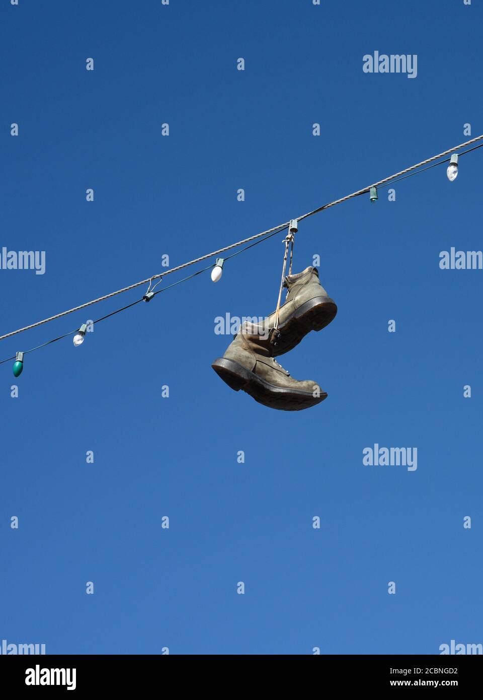 Schuhe und Stiefel hängen an einem elektrischen Draht, der über eine Straße im ländlichen Madrid, New Mexico USA, führt Stockfoto