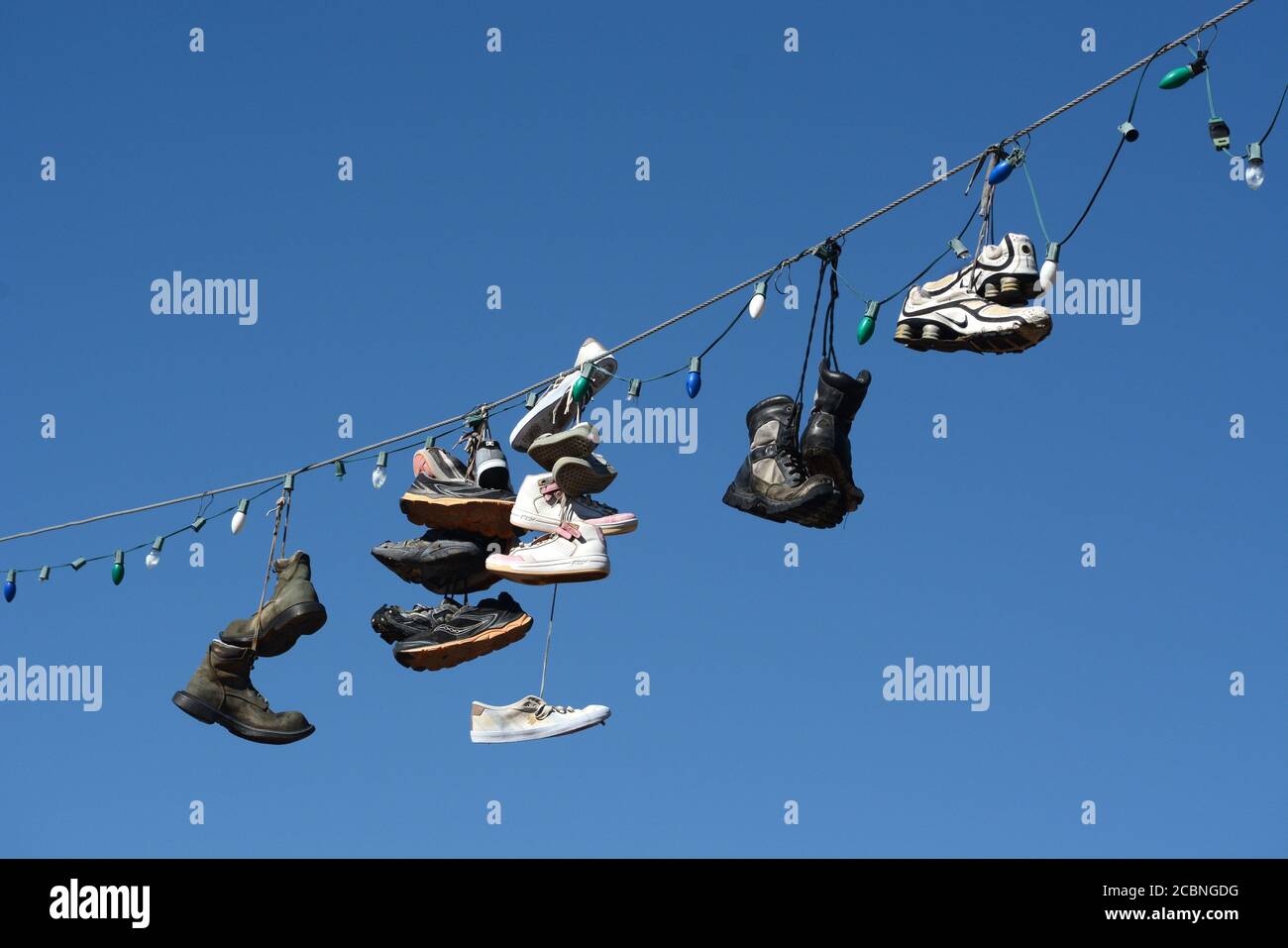 Schuhe und Stiefel hängen an einem elektrischen Draht, der über eine Straße im ländlichen Madrid, New Mexico USA, führt Stockfoto