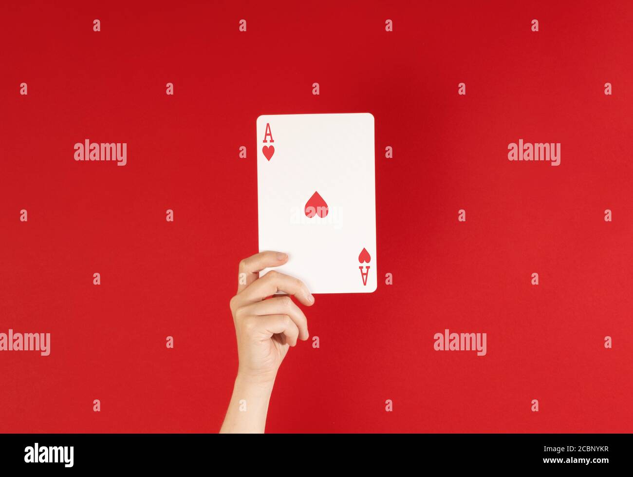 Ass der Herzen, Hand hält Spielkarte vor einem tiefen roten Hintergrund, mit Kopierraum Stockfoto