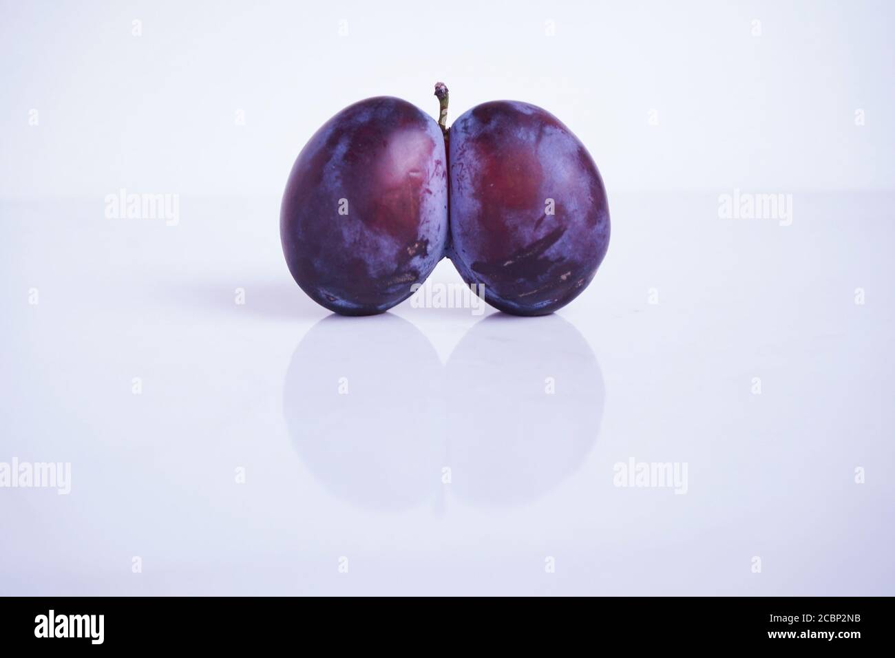 Nahaufnahme hässliche Pflaume. Verwöhnte Pflaume in Herzform auf weißem Hintergrund. Hässliche Früchte. Lustiges Essen. Verdorbenes Essen. Trendy hässliches Essenkonzept Stockfoto