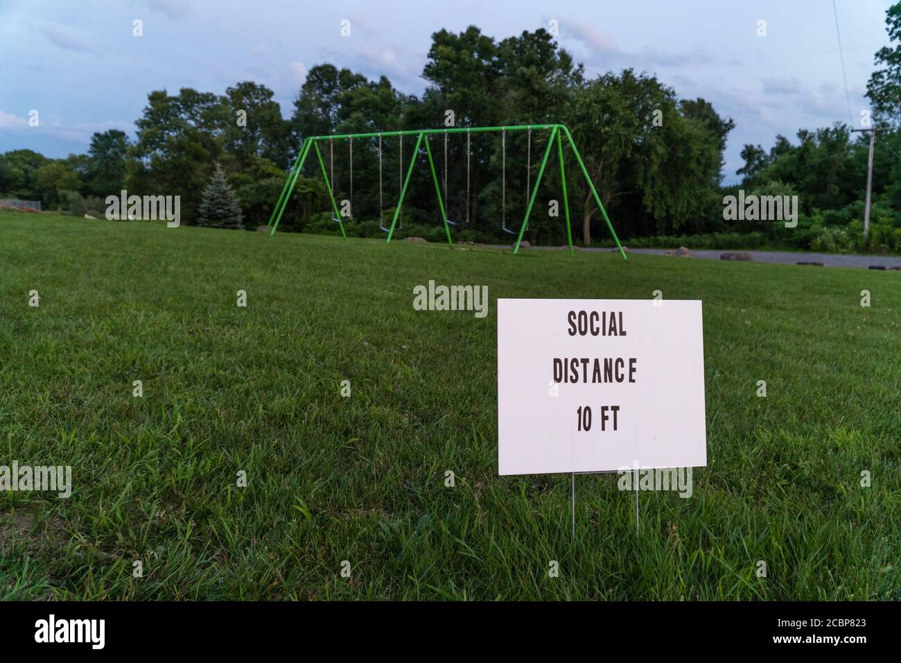 Schild mit Angabe sozialer Abstand 10 Fuß auf leerem Spielplatz mit Swingset im Hintergrund Stockfoto