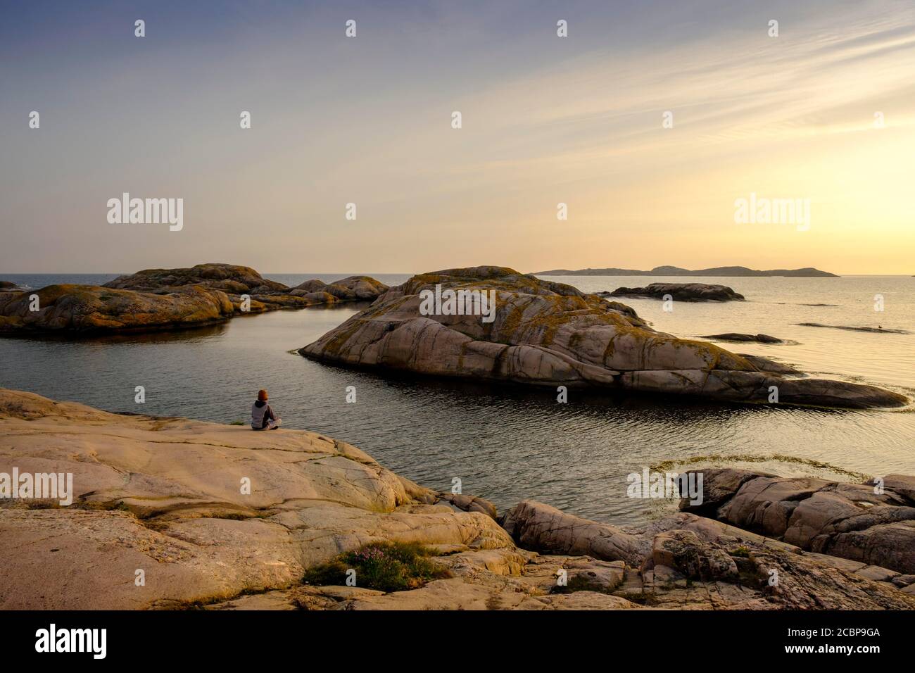 Junger Mann sitzt auf der Schärenküste, Schärenlandschaft, Naturschutzgebiet, Tjurpannans Naturschutzgebiet, in der Nähe von Grebbestrand, Archipel Stockfoto