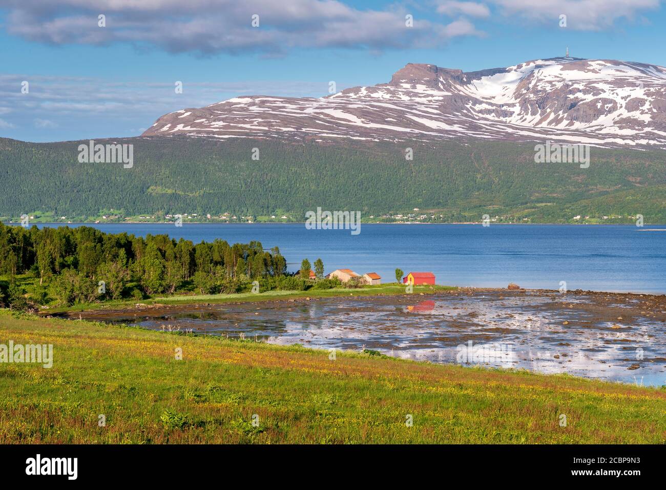 Holzhaus am Fjord, schneebedeckte Bergspitzen im Hintergrund, Senja Insel, Botnhamn, Troms, Norwegen Stockfoto