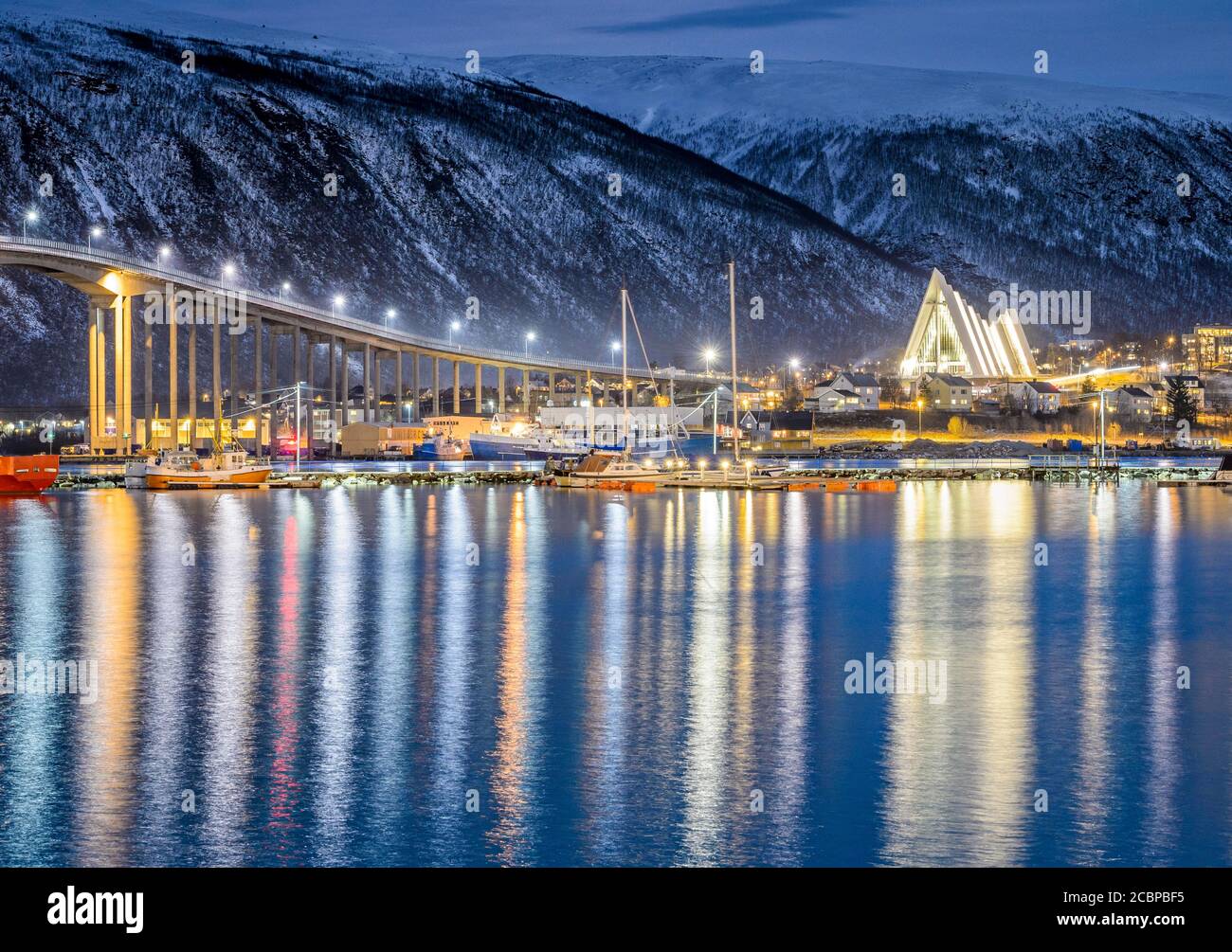 Blick über den Hafen und die Stadt mit Tromsobrua oder Tromso Brücke, hinten Tromsdalen Kirche, Arktisches Meer Kathedrale, Ishavskatdralen, in der Dämmerung Stockfoto