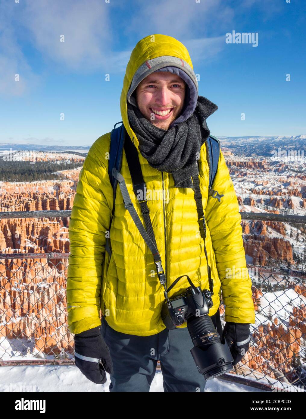 Porträt, junger Mann in Winterkleidung mit Kamera am Aussichtspunkt, felsige Landschaft mit Hoodoos im Winter, Rim Trail, Bryce Canyon National Park Stockfoto