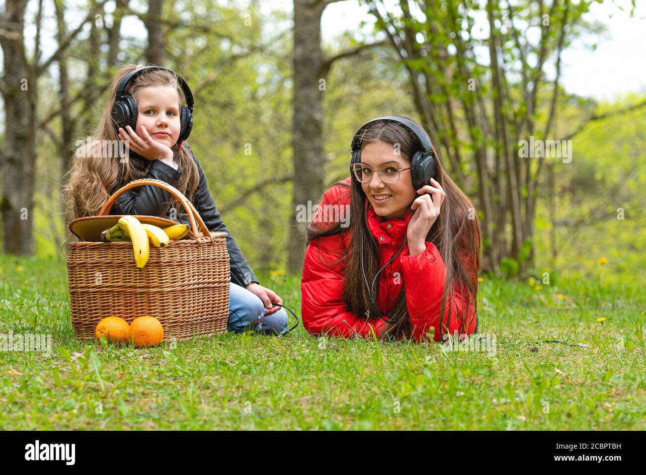 An einem sonnigen Frühlingstag ruhen zwei Schwestern im Park neben dem Picknickkorb auf dem Gras und hören Musik, Konzept für Lifestyle und Freizeit Stockfoto