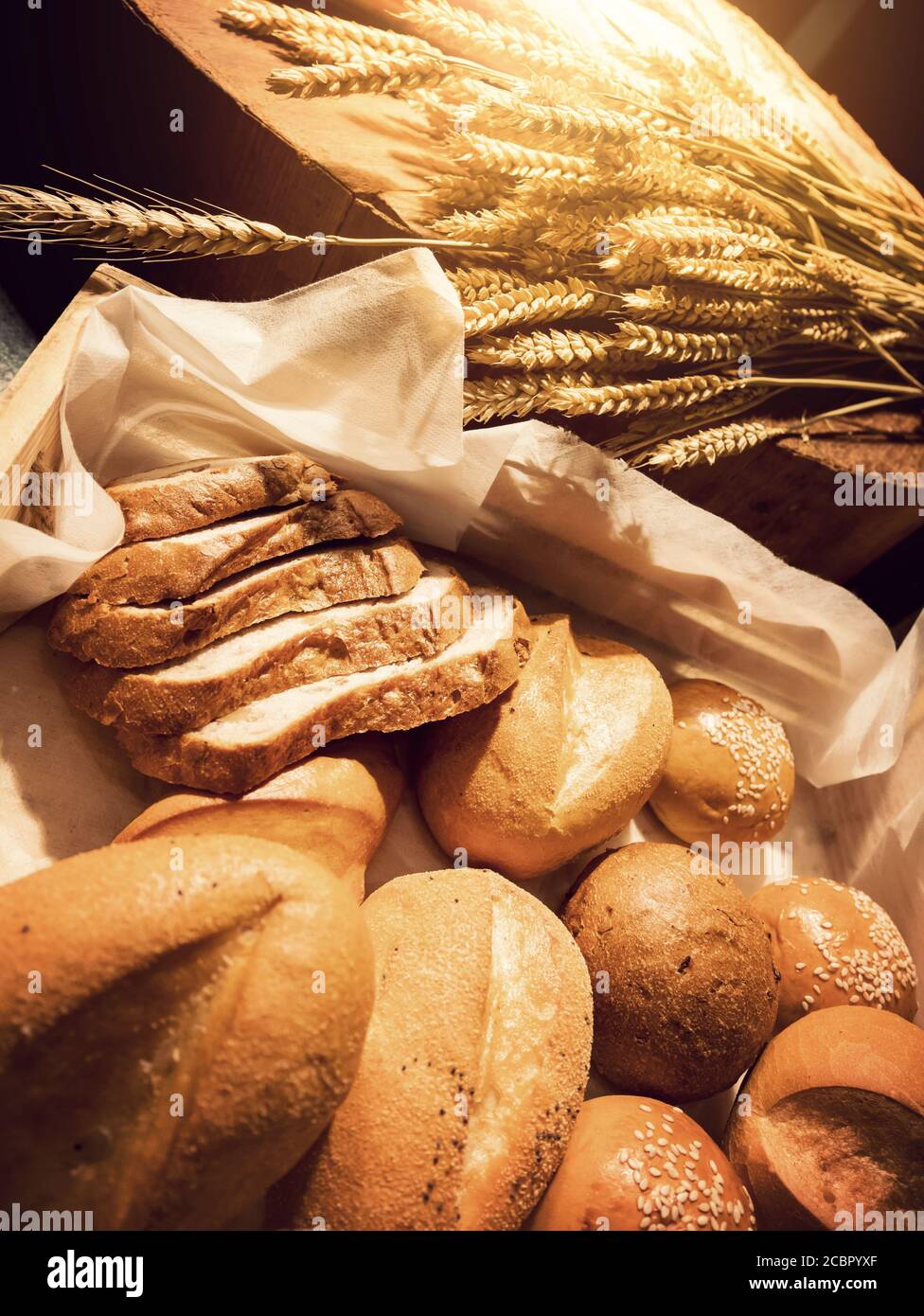 Hausgemachtes Bäckerkonzept: Frisches Brot und Weizen auf dem Holztisch mit warmem Licht Stockfoto