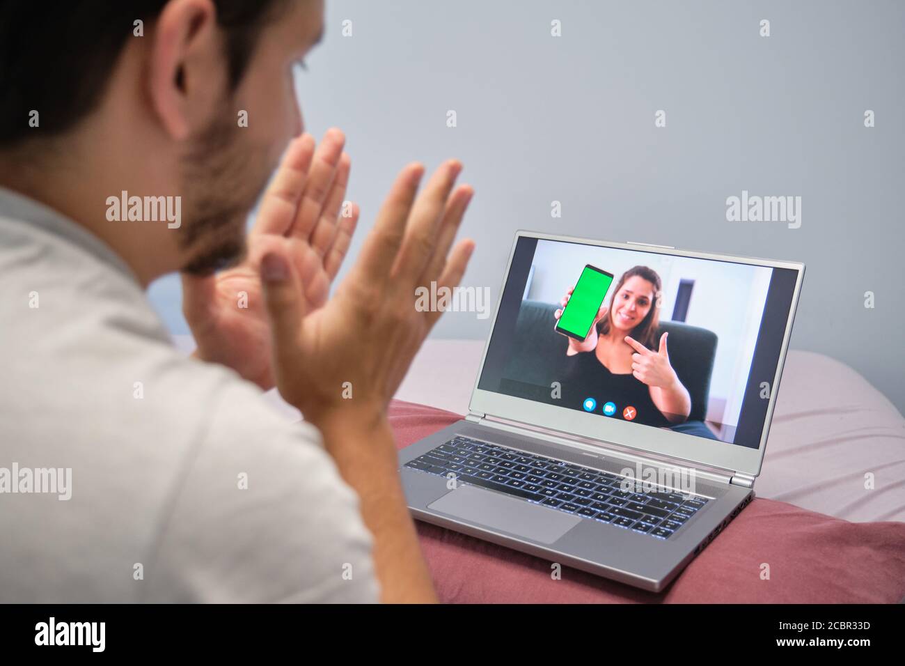 Junger Mann klatscht und spricht mit einer jungen Frau, die ihm am Telefon etwas zeigt. Junges Paar Online-Anruf-Konzept. Stockfoto