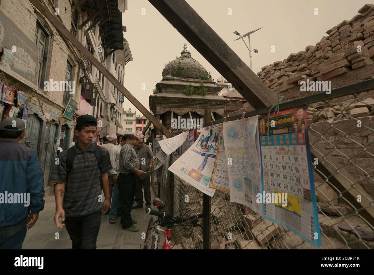 Fußgänger, die auf einer Gasse zwischen Wohngebiet und einem Kulturdenkmal gehen, das von den Erdbeben von 2015 in Kathmandu, Nepal, betroffen ist. Stockfoto