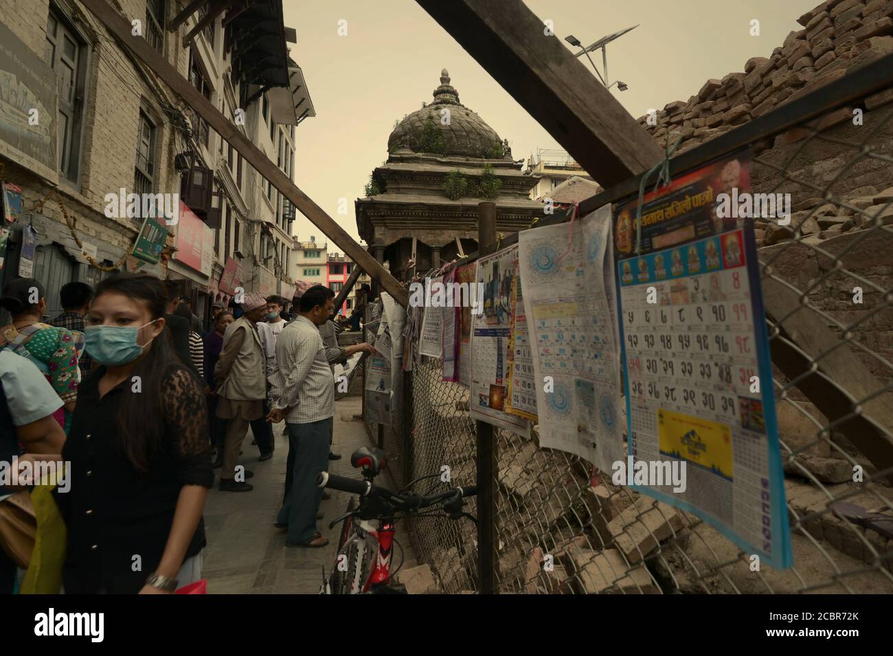 Ein Fußgänger mit Gesichtsmaske auf einer Gasse zwischen Wohngebiet und einem Kulturdenkmal, das von den Erdbeben von 2015 in Kathmandu betroffen ist. Stockfoto