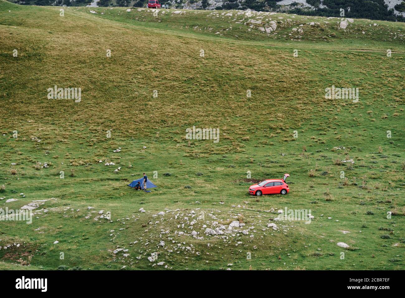 Zabljak, Montenegro - 23. juli 2020: Touristen auf einem roten Auto, legte ein Touristenzelt auf dem grünen Gras, in den Bergen im Norden von Montenegro, in der Stockfoto