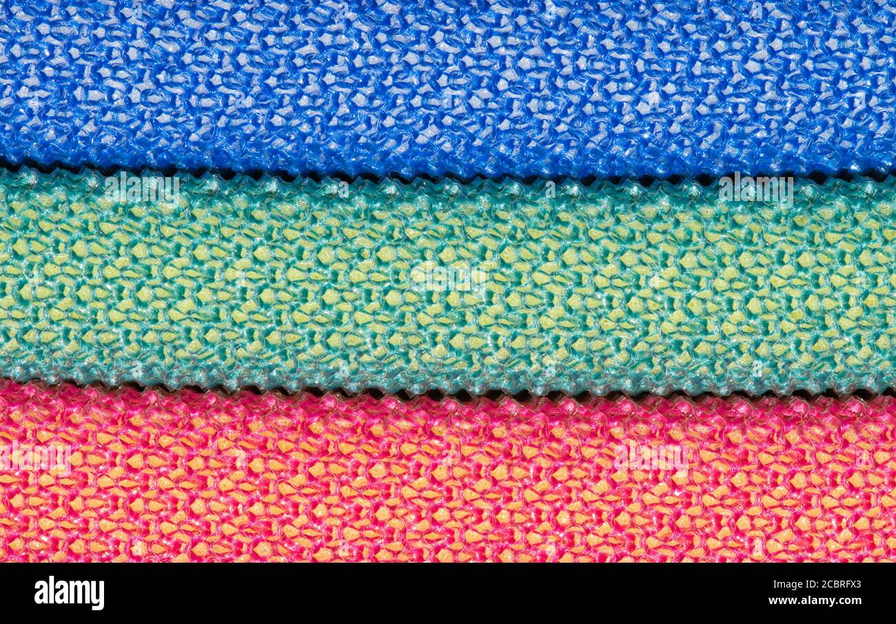 Drei farbige Scheuerschwämme horizontal aufgestapelt, blau grün und rot. Abstraktes Vollformat-Makrobild mit Kopierbereich. Stockfoto