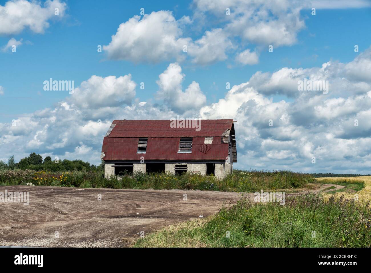 Ein lange verlassene Bauernhaus .gebrochene Fenster, verfallene Schindeln und ein bröckelnder Ziegelkamin mit einem blauen Himmel und grasbewachsenen Vordergrund. Stockfoto