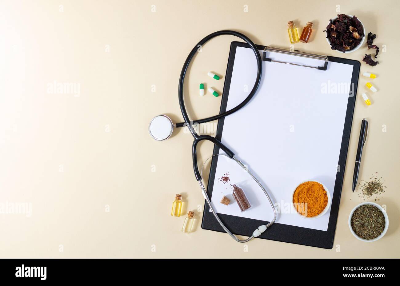 Alternative Medizin, Naturopathie oder ayurveda-Konzept. Leere Zwischenablage mit Stethoskop, verschiedenen Heilkräutern, Gewürzen, Kapseln und gesunden Ölen auf Stockfoto