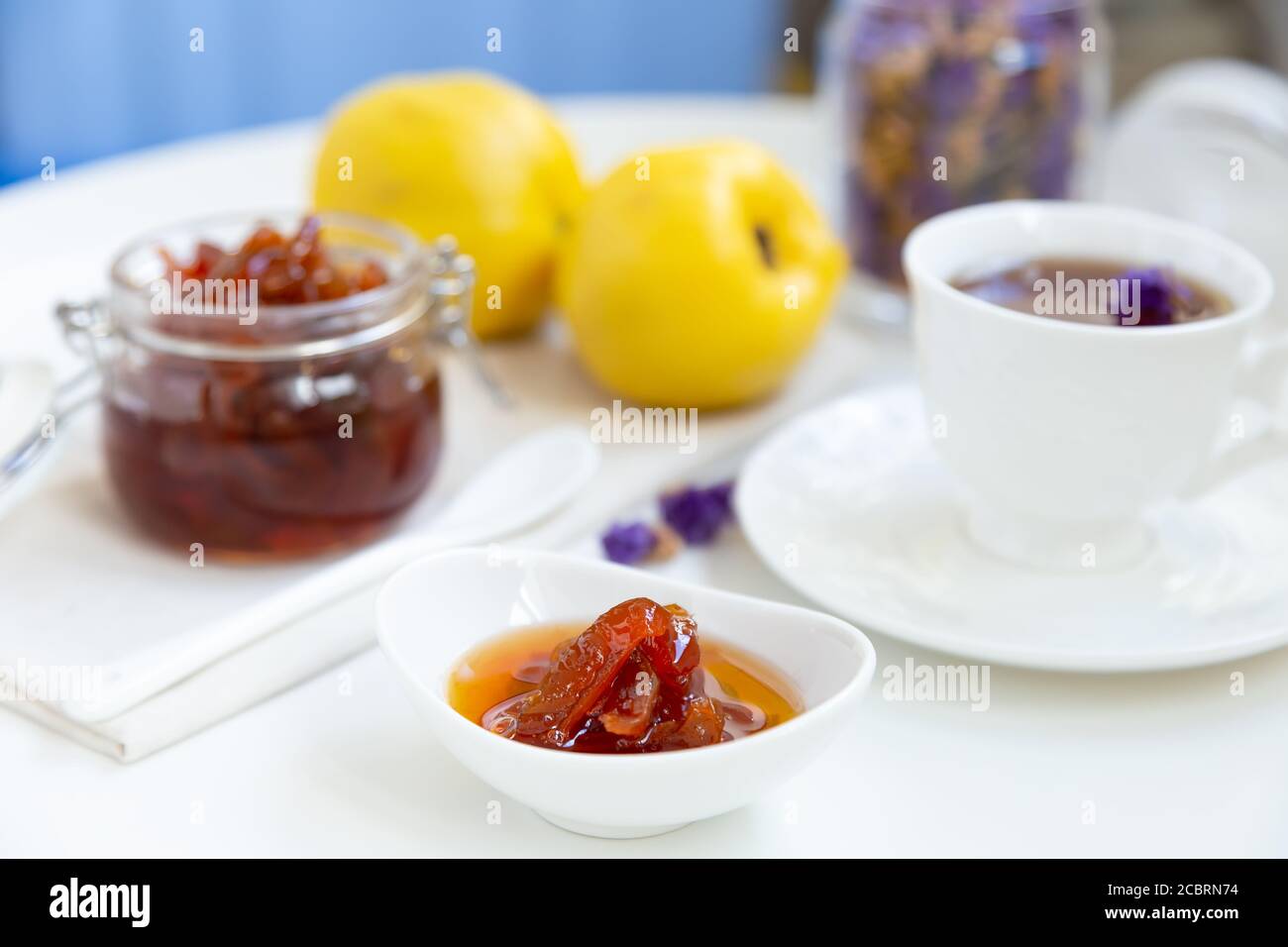 Hausgemachte Quitten-Marmelade in einer Porzellanschüssel mit einer Tasse Tee. Im Hintergrund ist ein Glas mit Marmelade und Quitte. Stockfoto