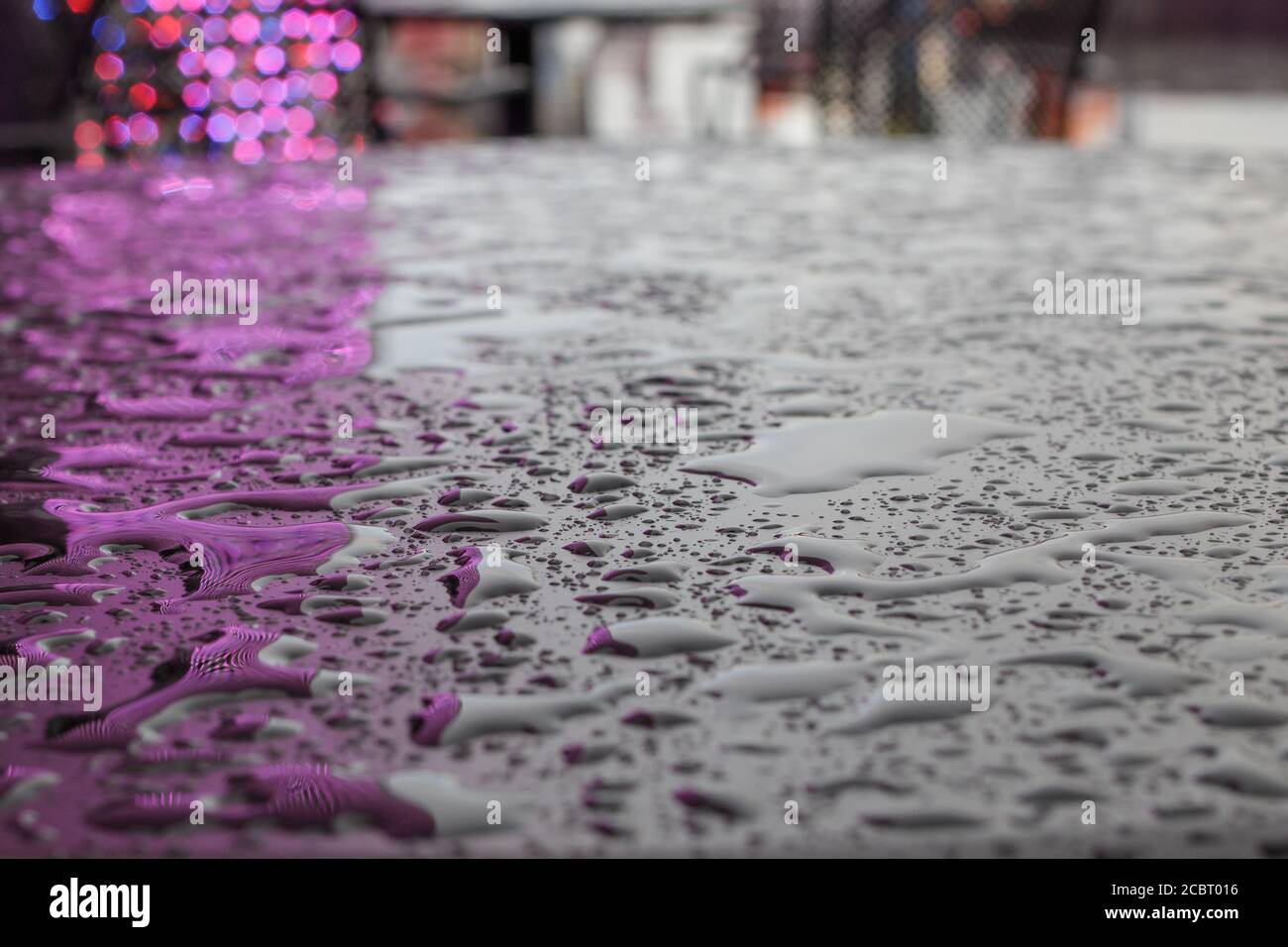 Textur. Tropfen oder kleine Wasserpfützen nach dem Regen auf einer glatten matten Oberfläche von dunkler Farbe, die das Licht der Beleuchtung reflektiert. Stockfoto