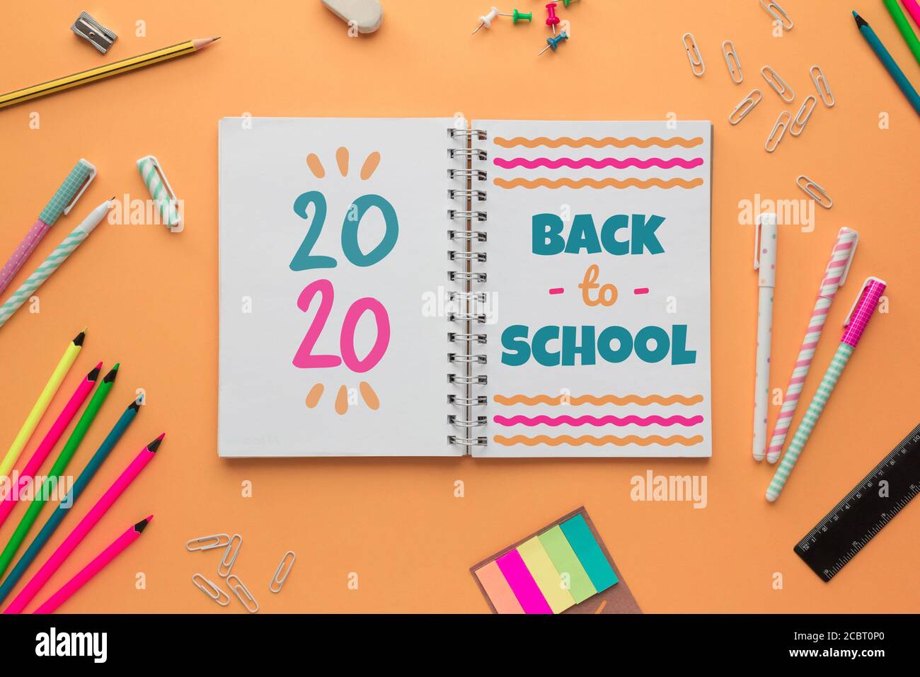 Stock Foto des Back to School Konzept mit einem Offenes Notizbuch mit Schriftzügen und einigen Schreibwaren auf einem Lachshintergrund Stockfoto