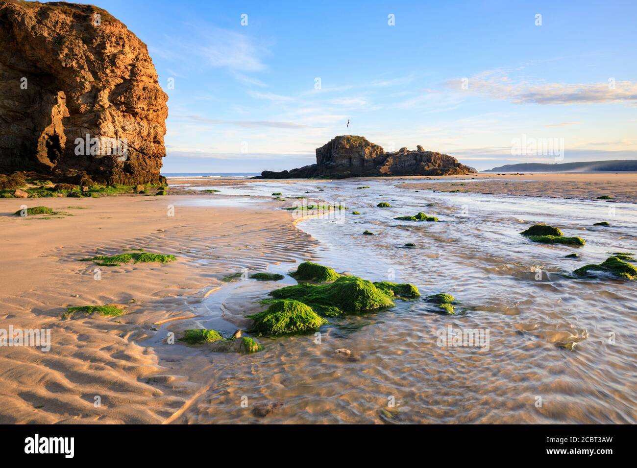 Der natürliche Meeresbogen und der Chapel Rock am Perranporth Beach in Cornwall wurden an einem Morgen Mitte Juli mit Sandmustern als Vordergrund-Interesse aufgenommen. Stockfoto
